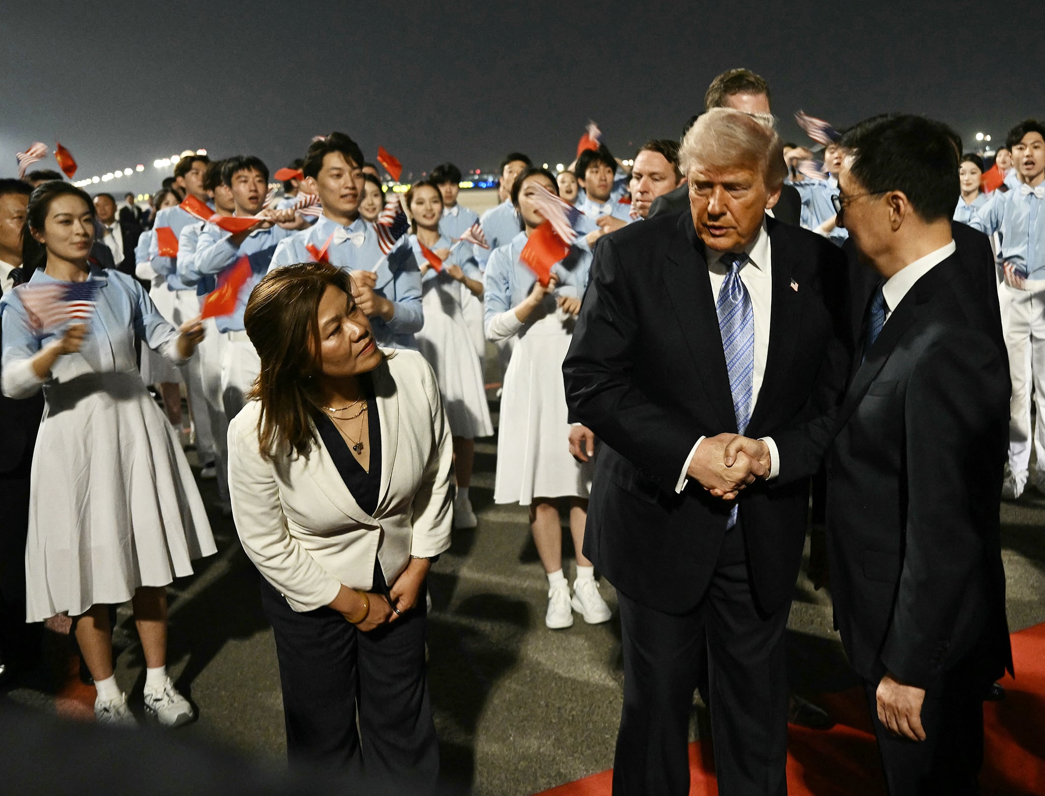 US President Donald Trump is greeted by China’s Vice President Han Zheng, with people waving US and China flags around them.