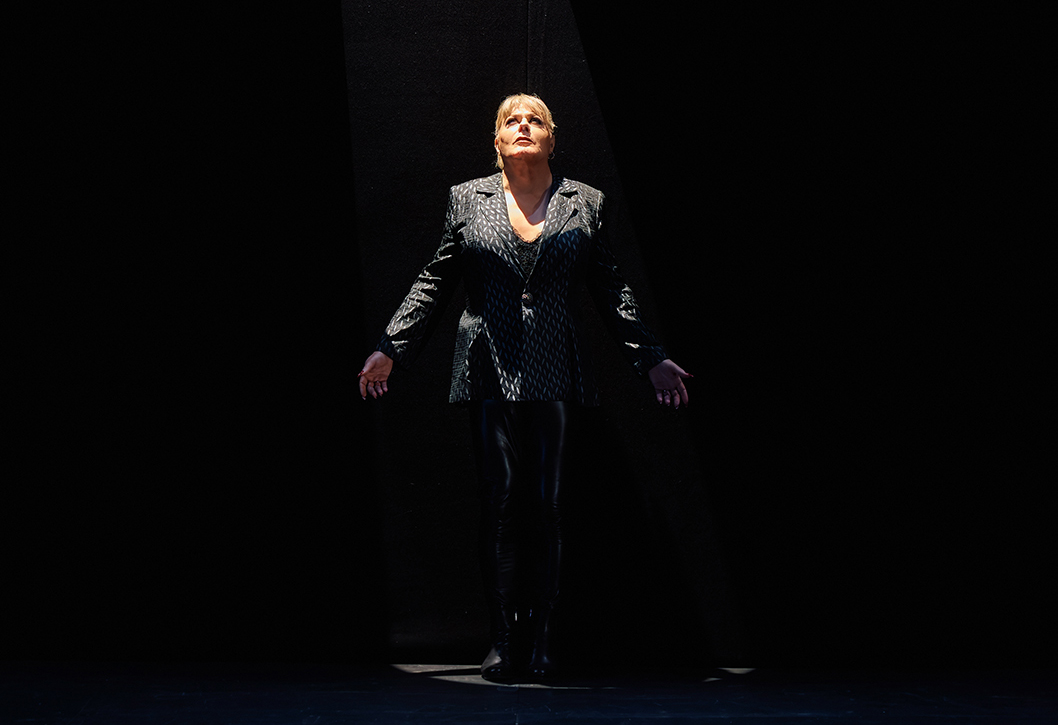 A person stands under the spotlight on a dark stage.