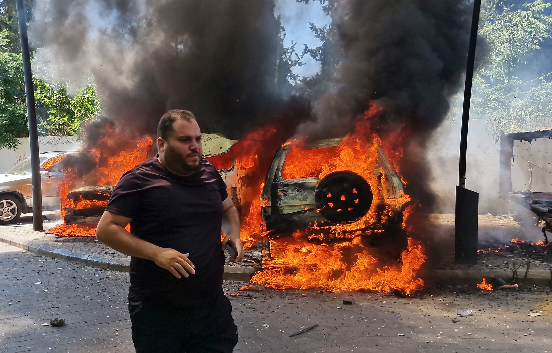 A man runs past burning cars following an Israeli air strike on the southern port city of Sidon, Lebanon.A