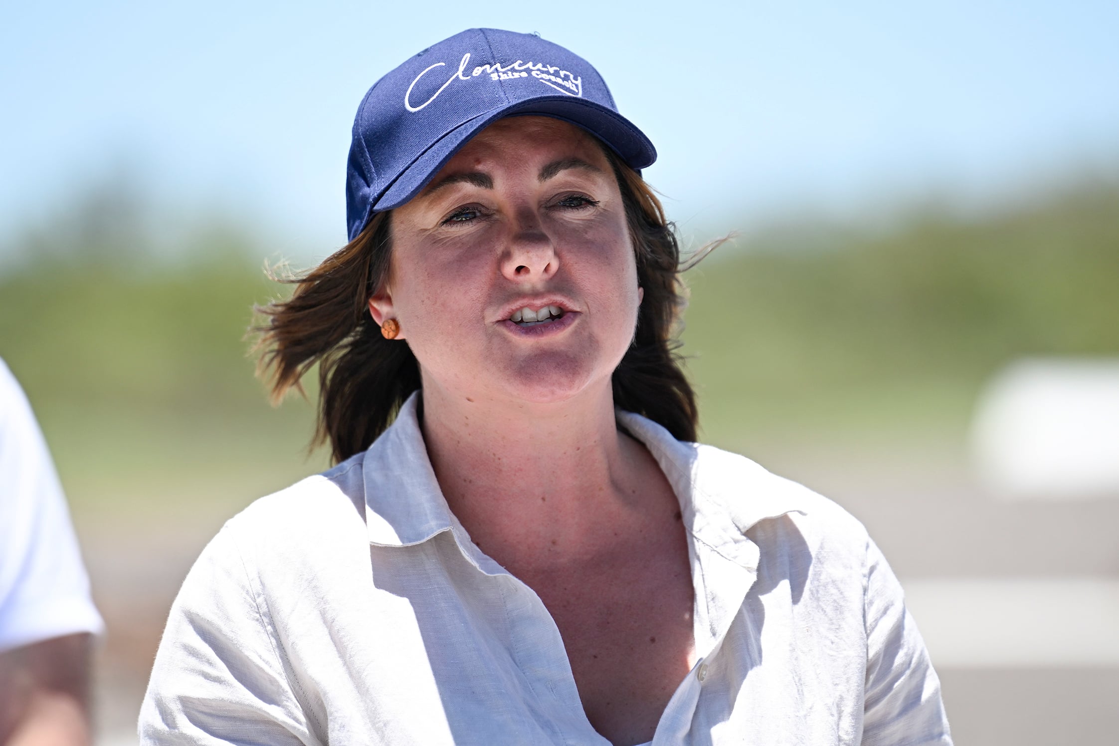 Kristy McBain outdoors in blue cap and white shirt.