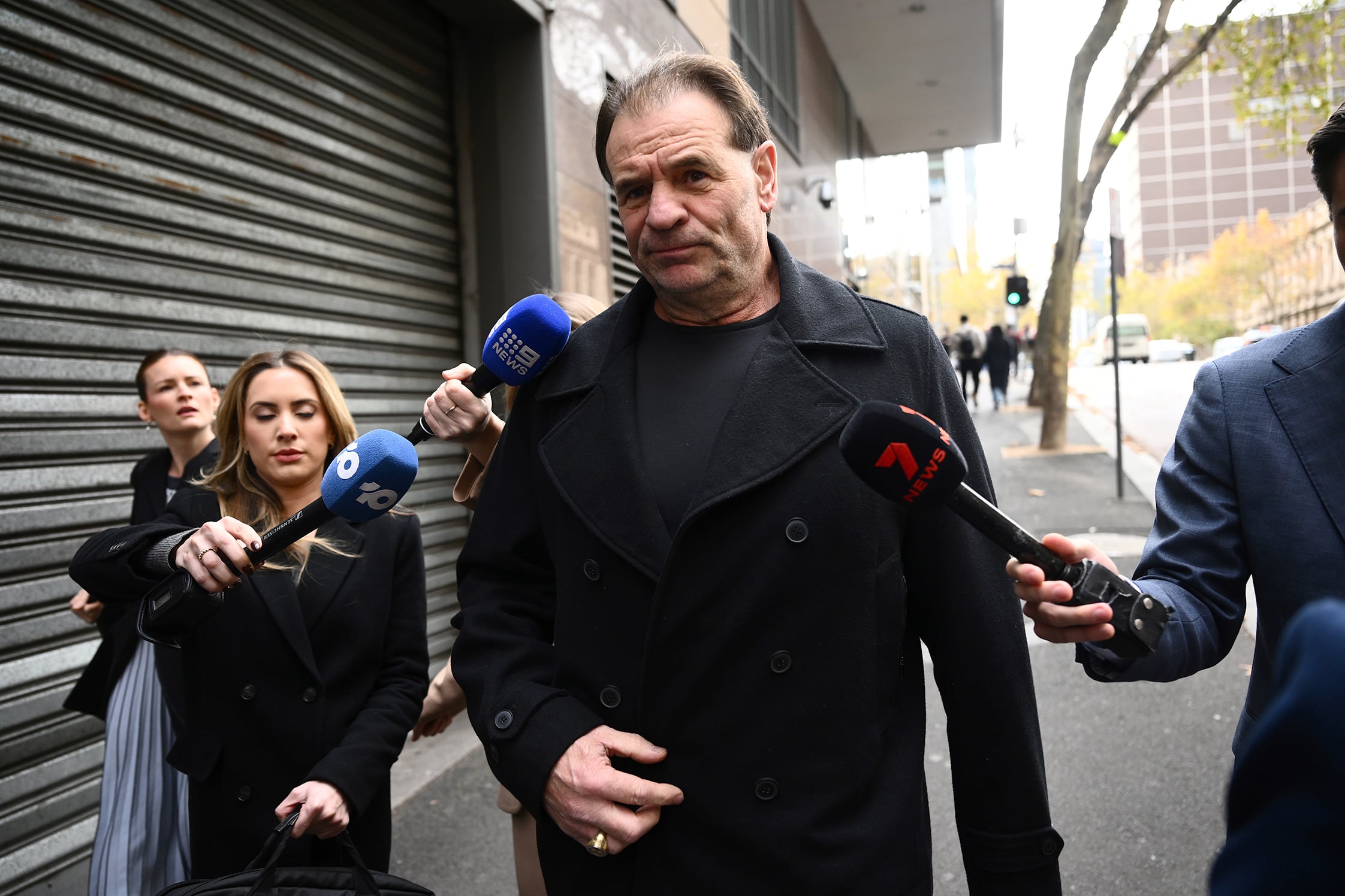 Man in black jacket walks through media pack.