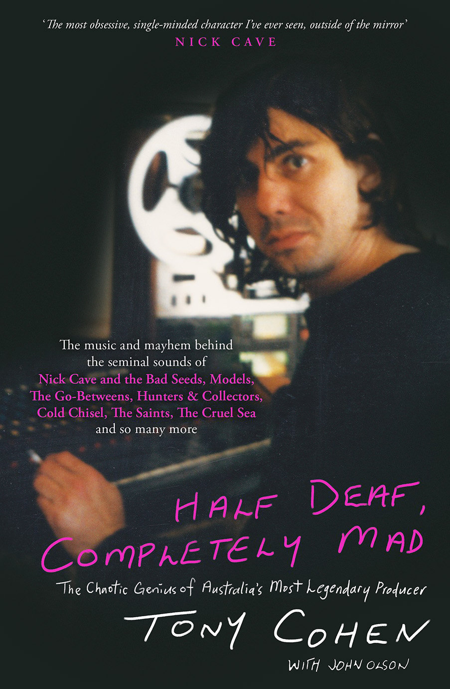 A middle-aged man with a mop of black hair sits a control board in a recording studio.