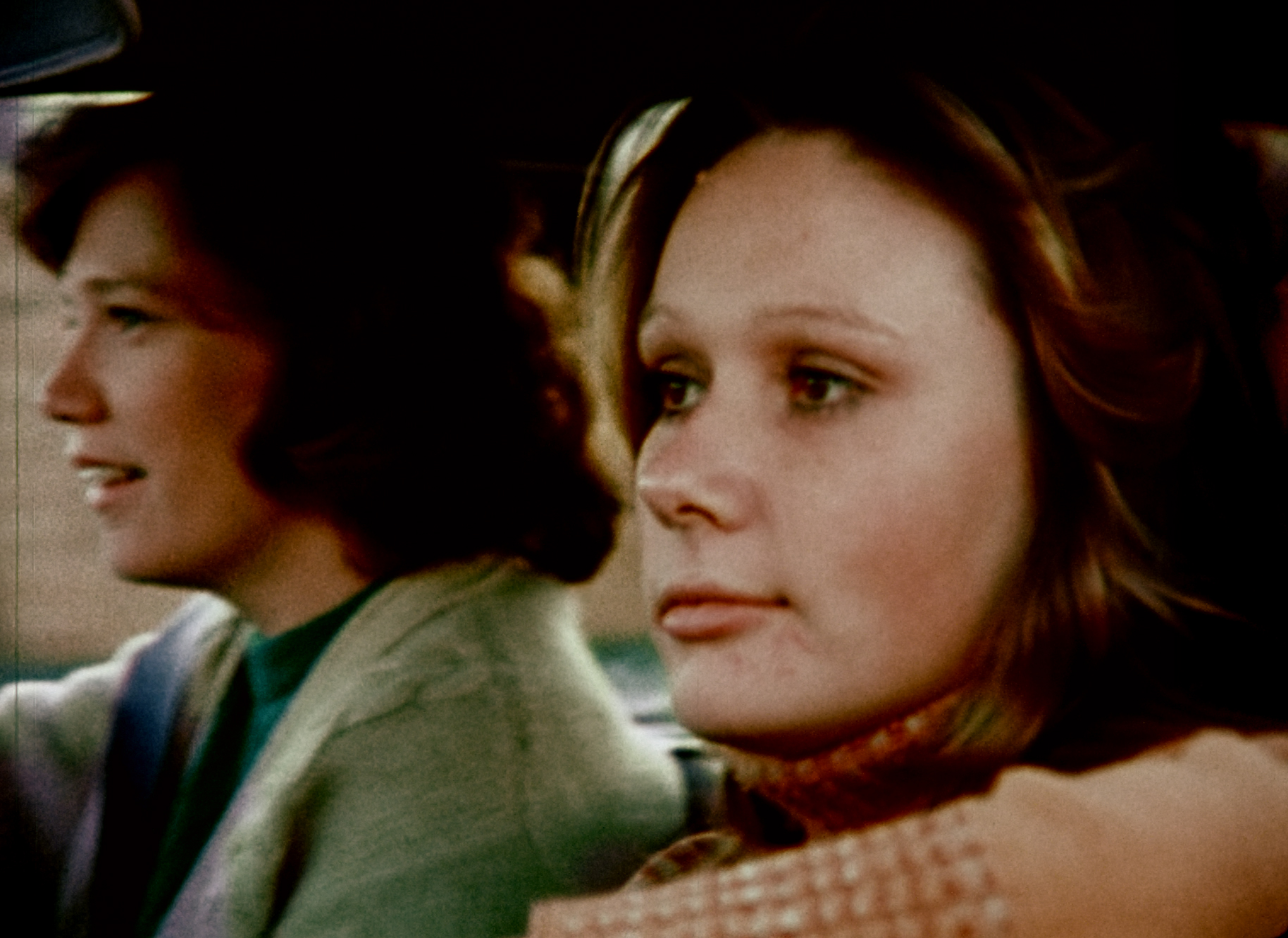 A young woman sits in the passenger side of a car with the window down.