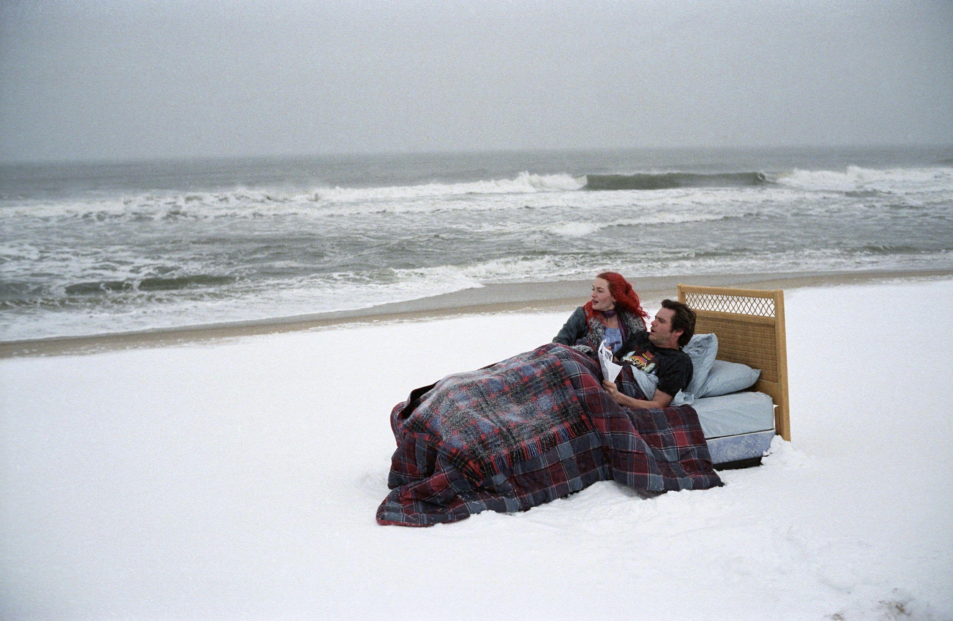 A man and a woman resting in a bed that sits on a snow-covered beach