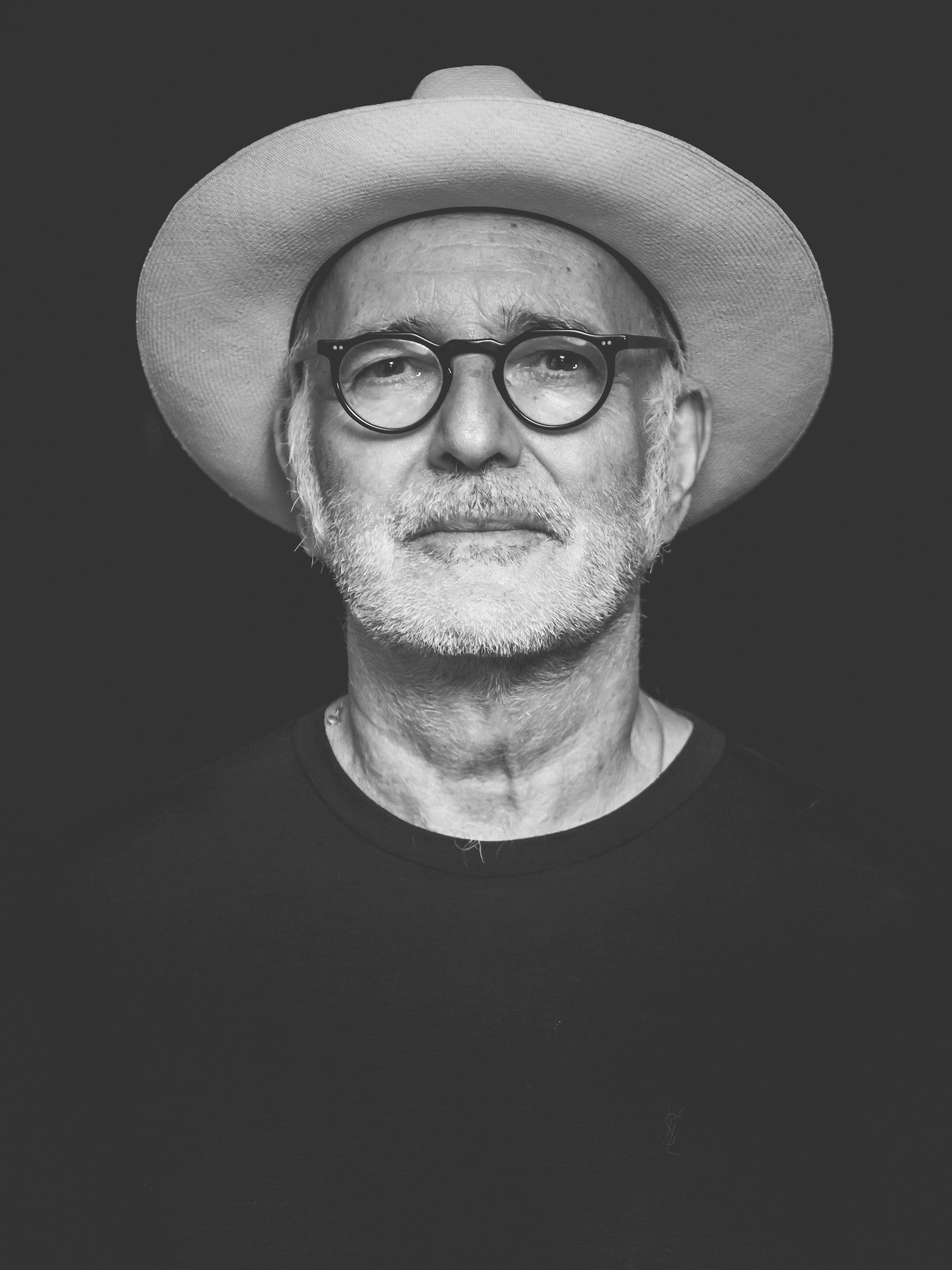 A grey bearded man wearing glasses and a hat.