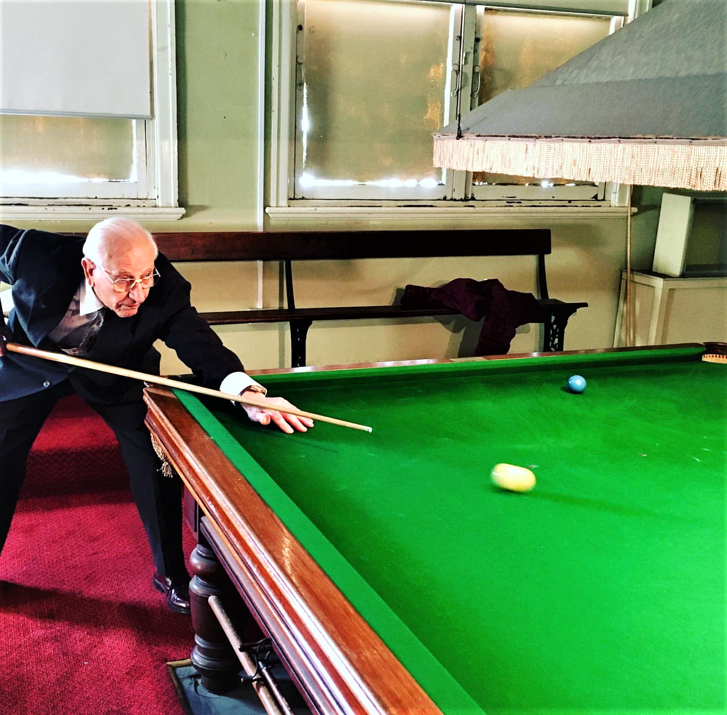 An elderly man in a suit playing a game of pool.