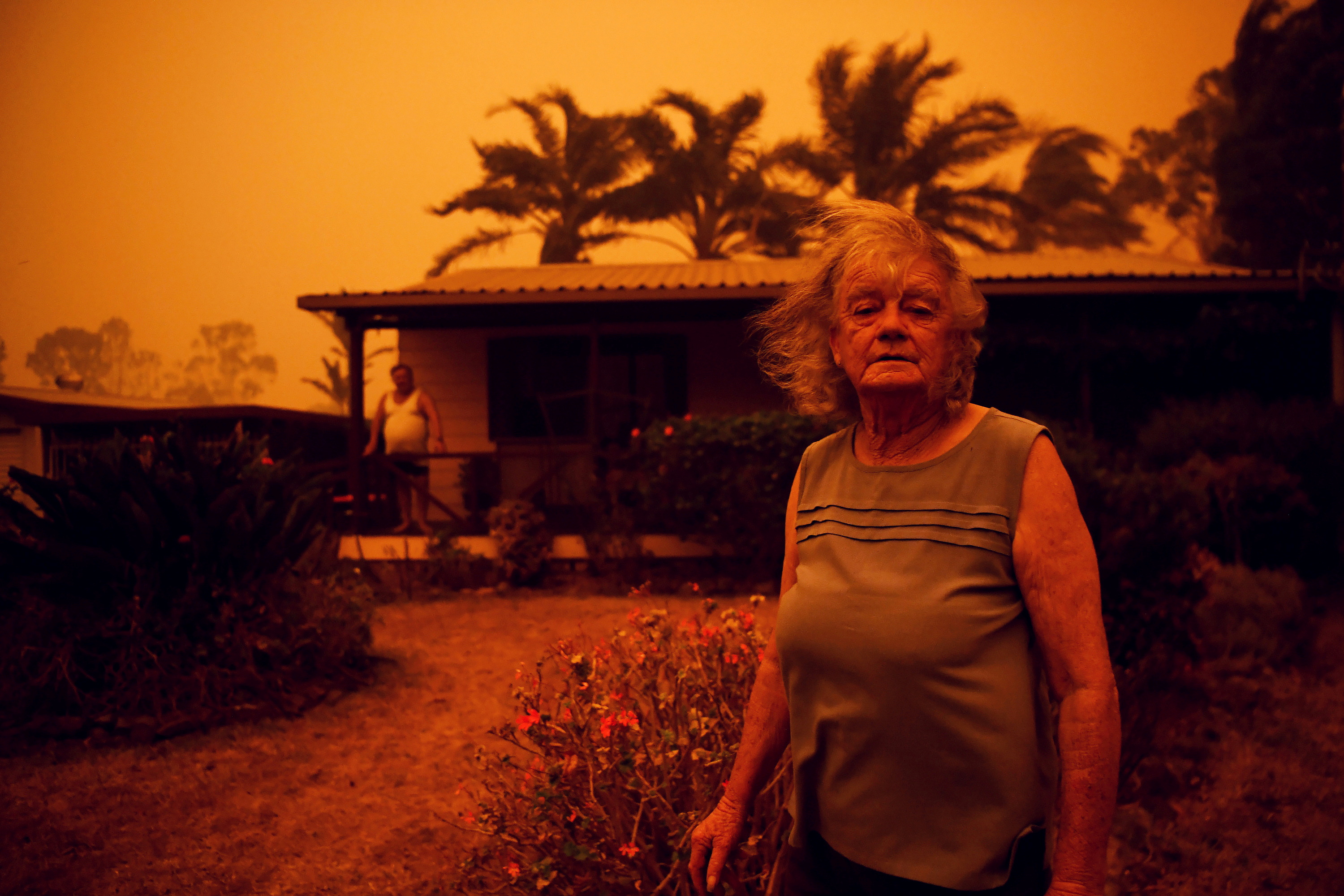 A woman standing in front of her property. the sky a stark orange.