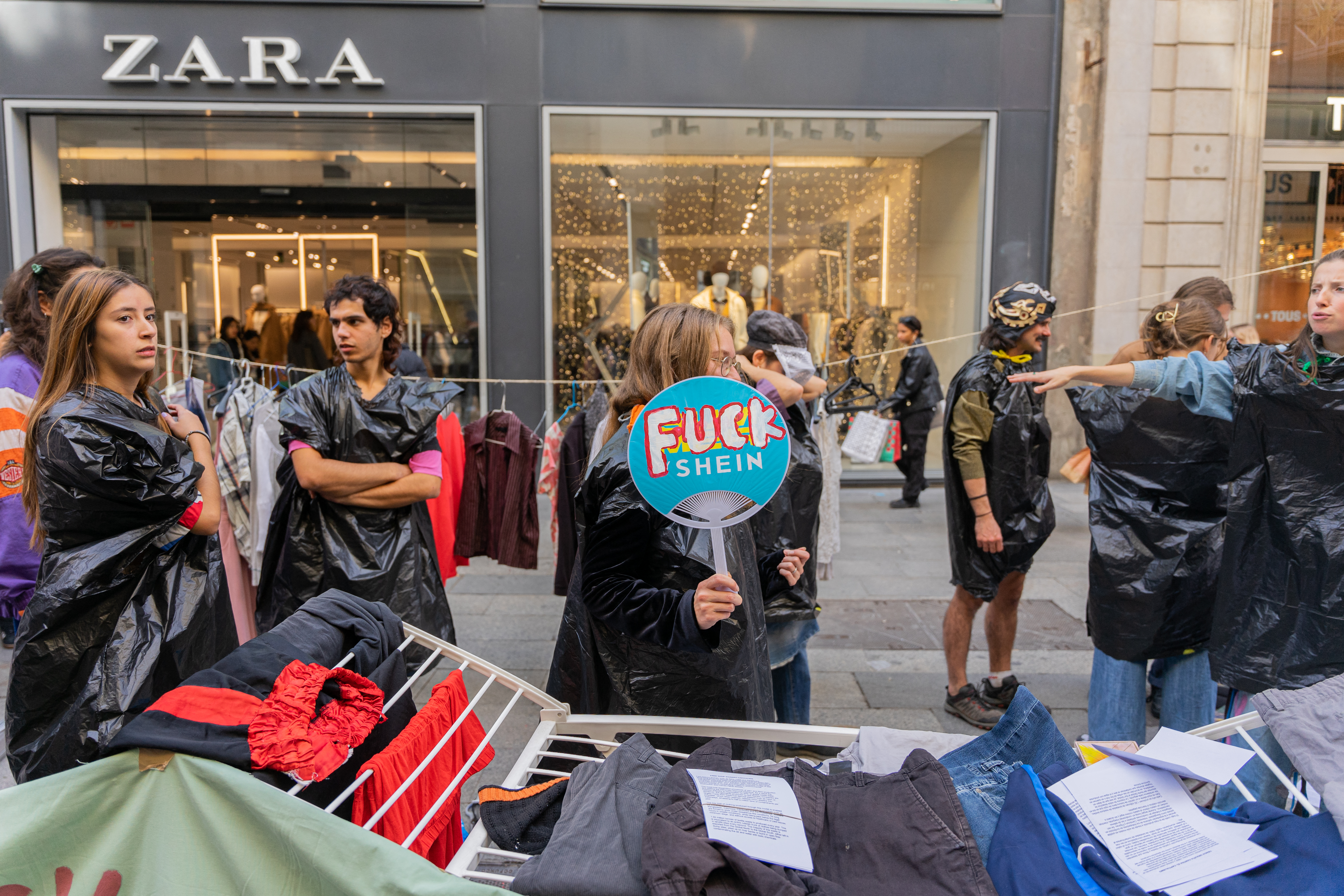 A woman holding an anti fast-fashion sign in front of a Zara store.
