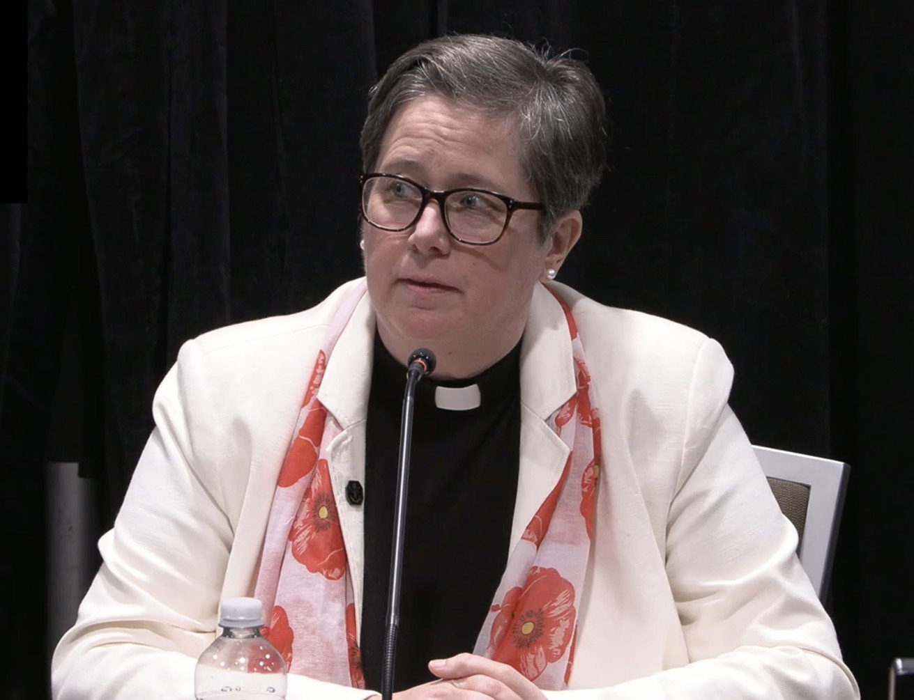 A woman with short hair and wearing glasses at a hearing.