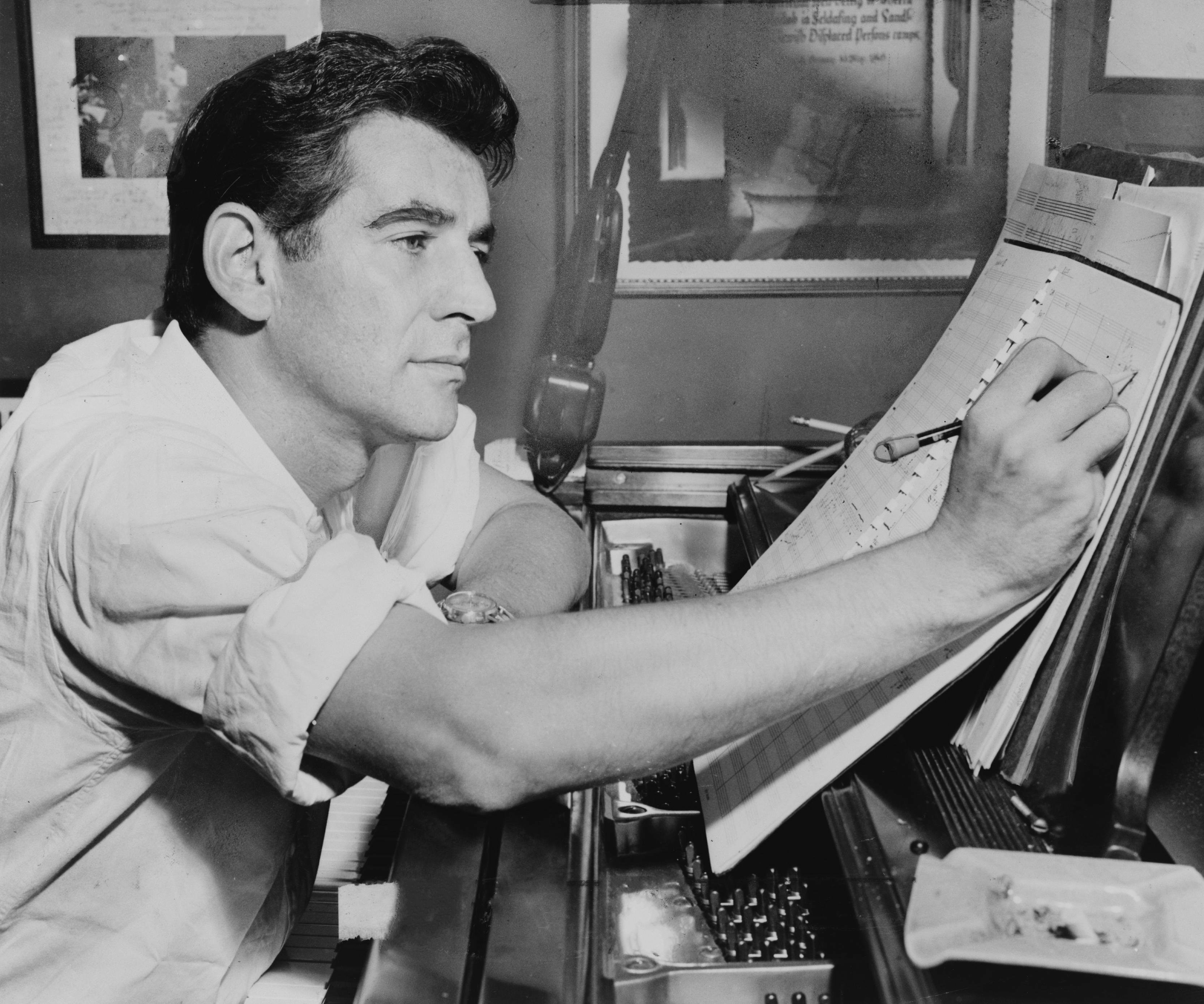 Black and white photograph of a man sitting at a piano, writing into a book.