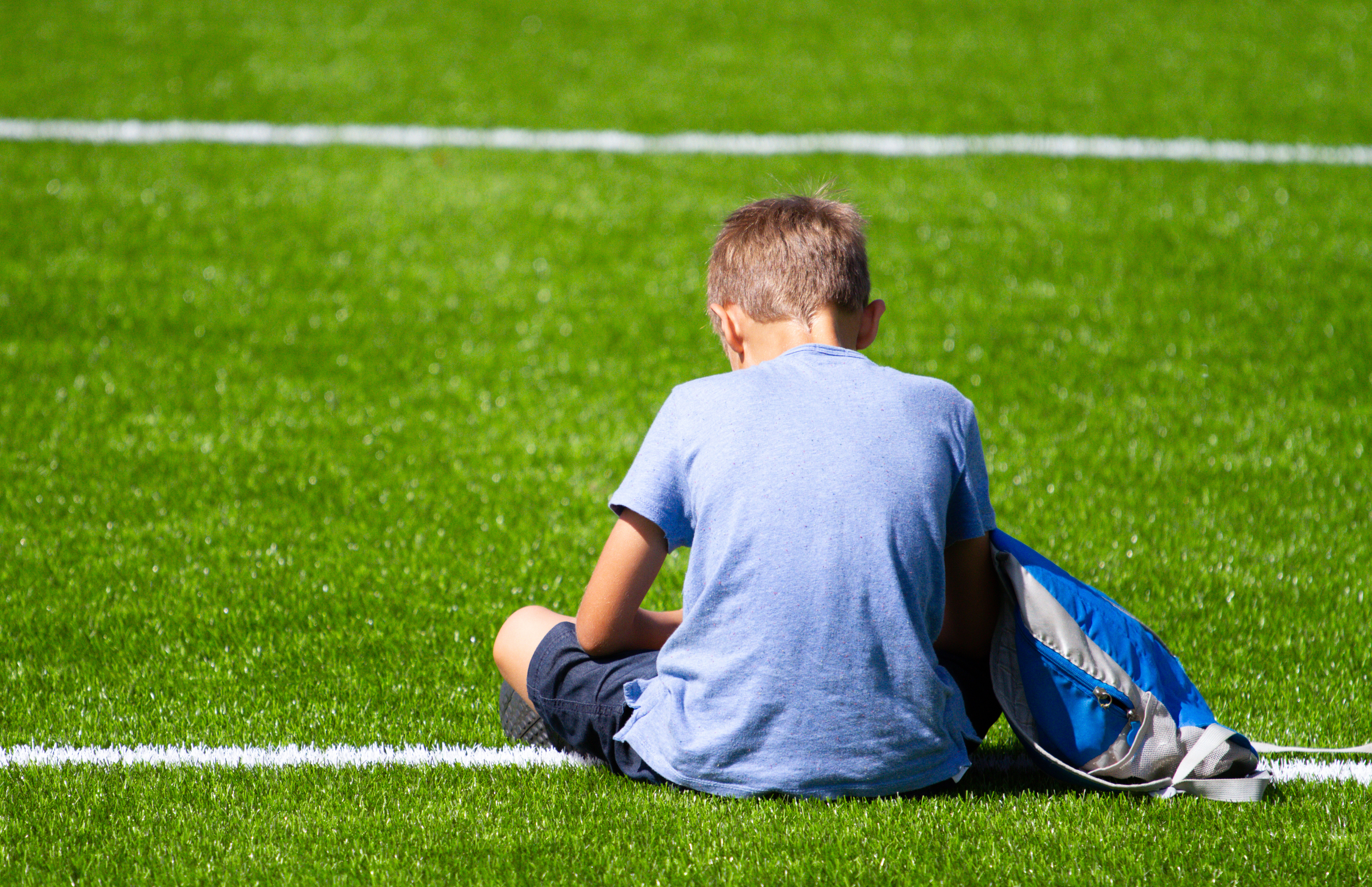 A young boy sits alone on a sporting field.