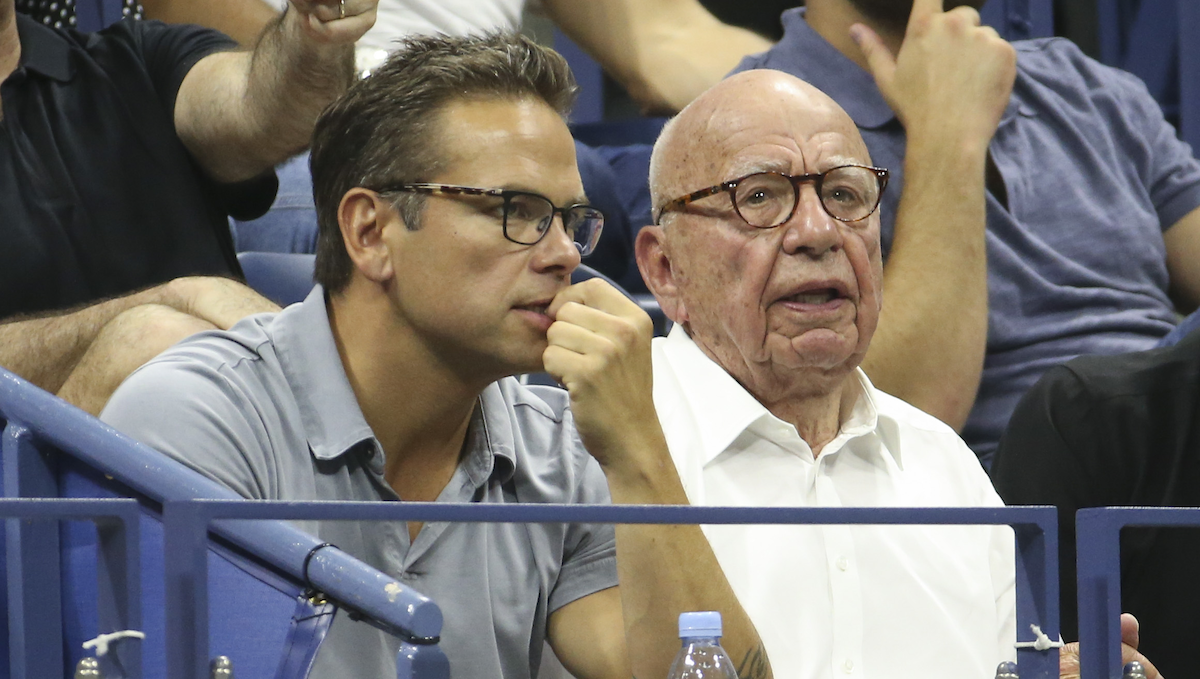 Lachlan Murdoch and Rupert Murdoch sit in the stands of an arena. 