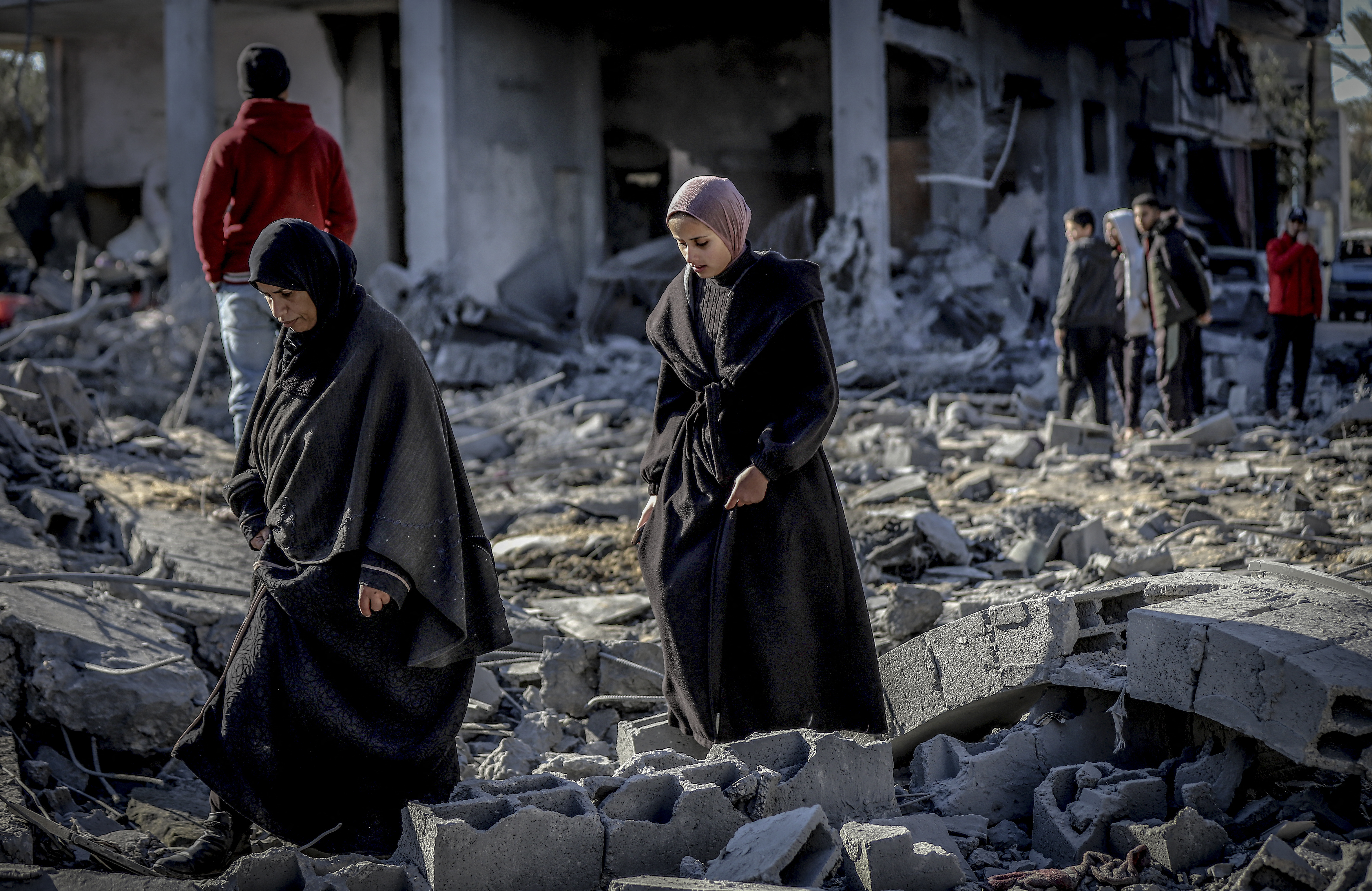 Palestinians pick their way across the ruins of a city.