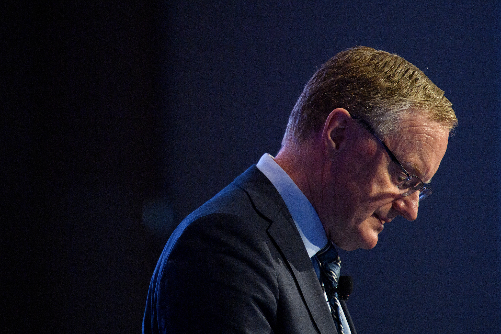 Philip Lowe wearing a suit and glasses, looking toward the ground.