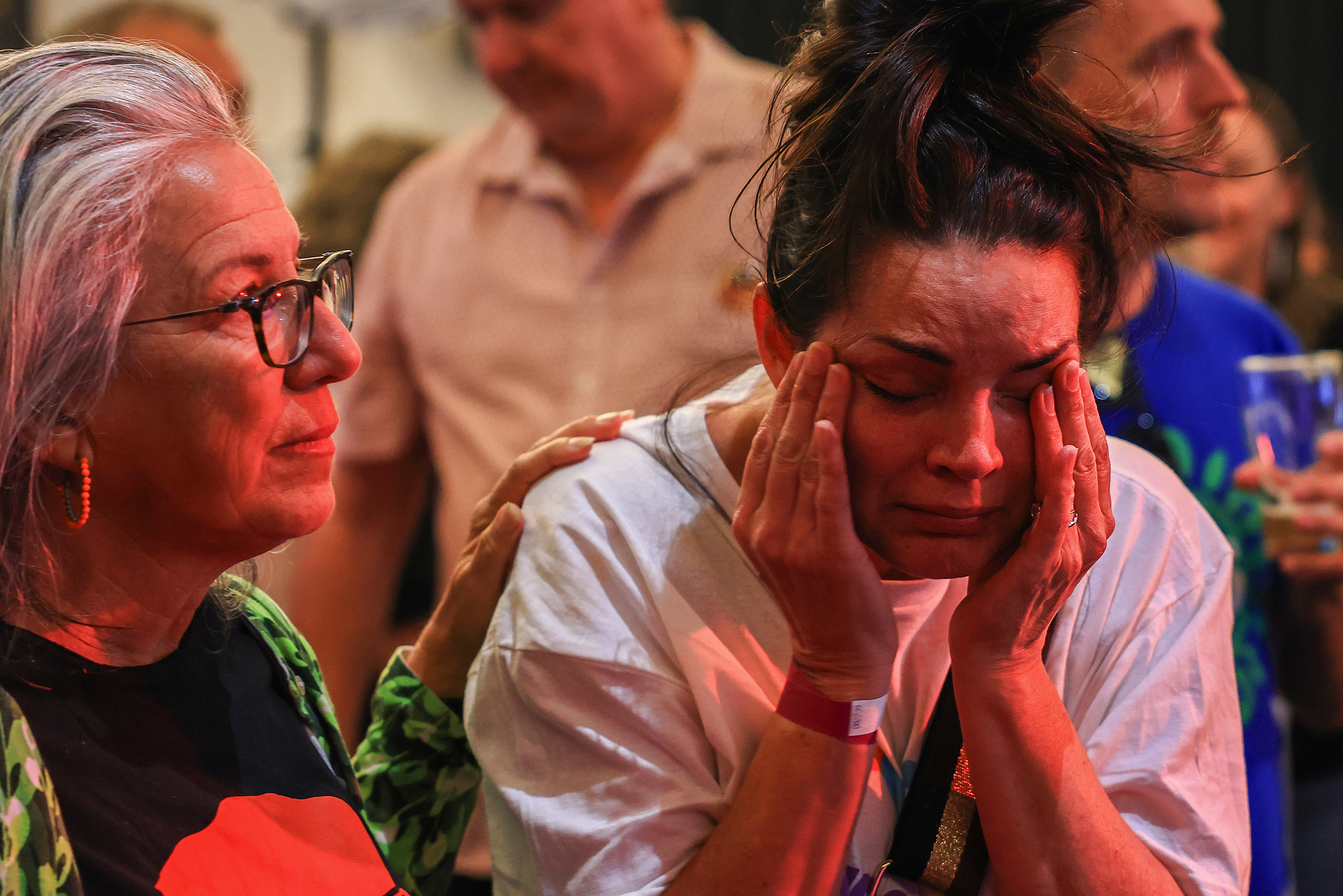 A woman consoles the woman beside her, who is crying.