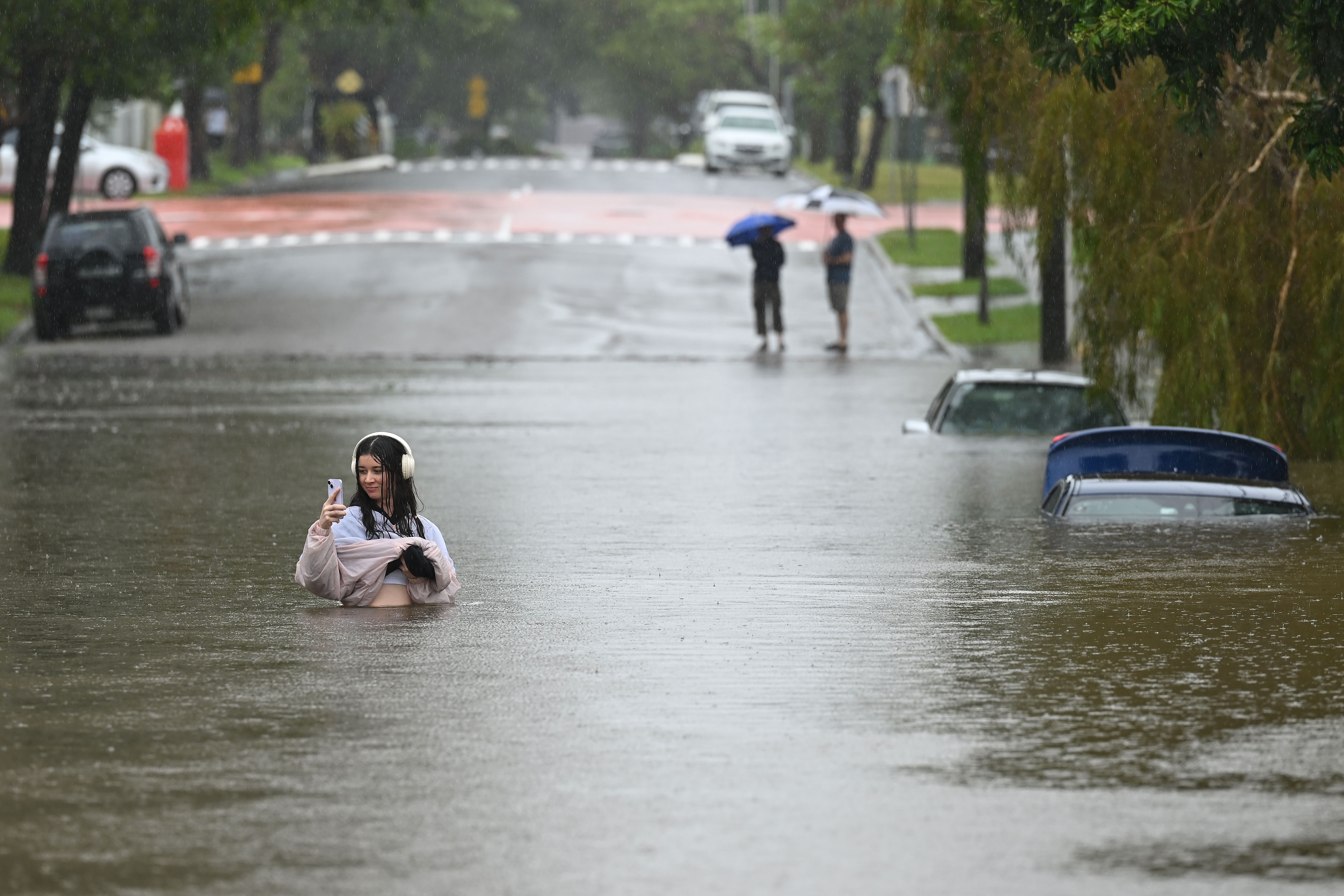 A young woman on her phone while standing on a flooded road.
