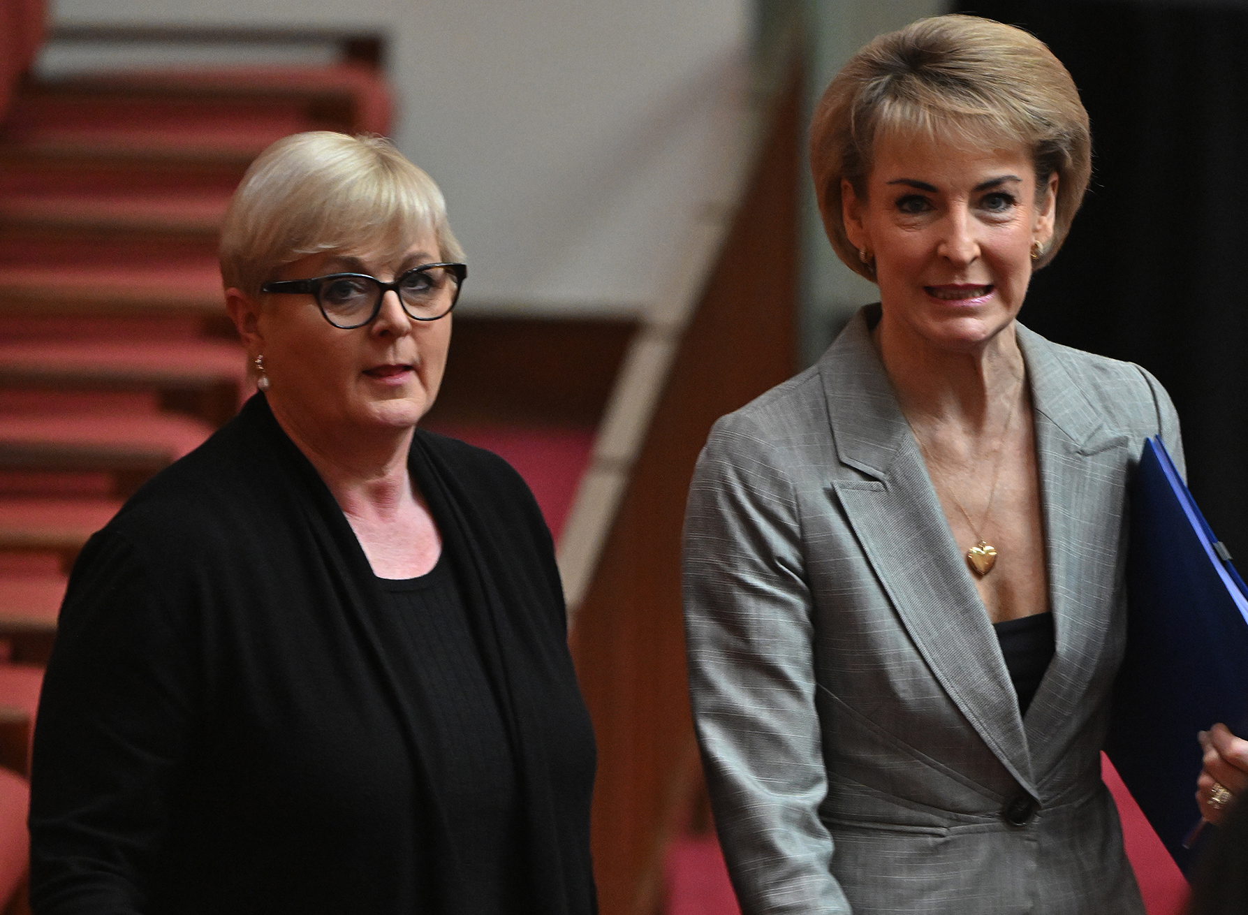 Two women with short hair walk through senate chamber.