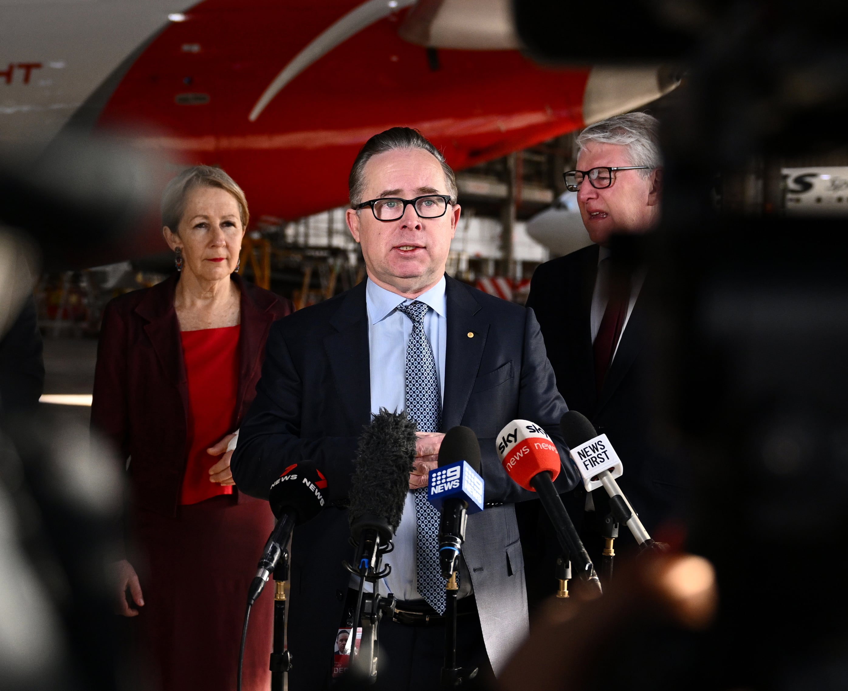 Alan Joyce speaks at a press conference with a Qantas plan behind him.