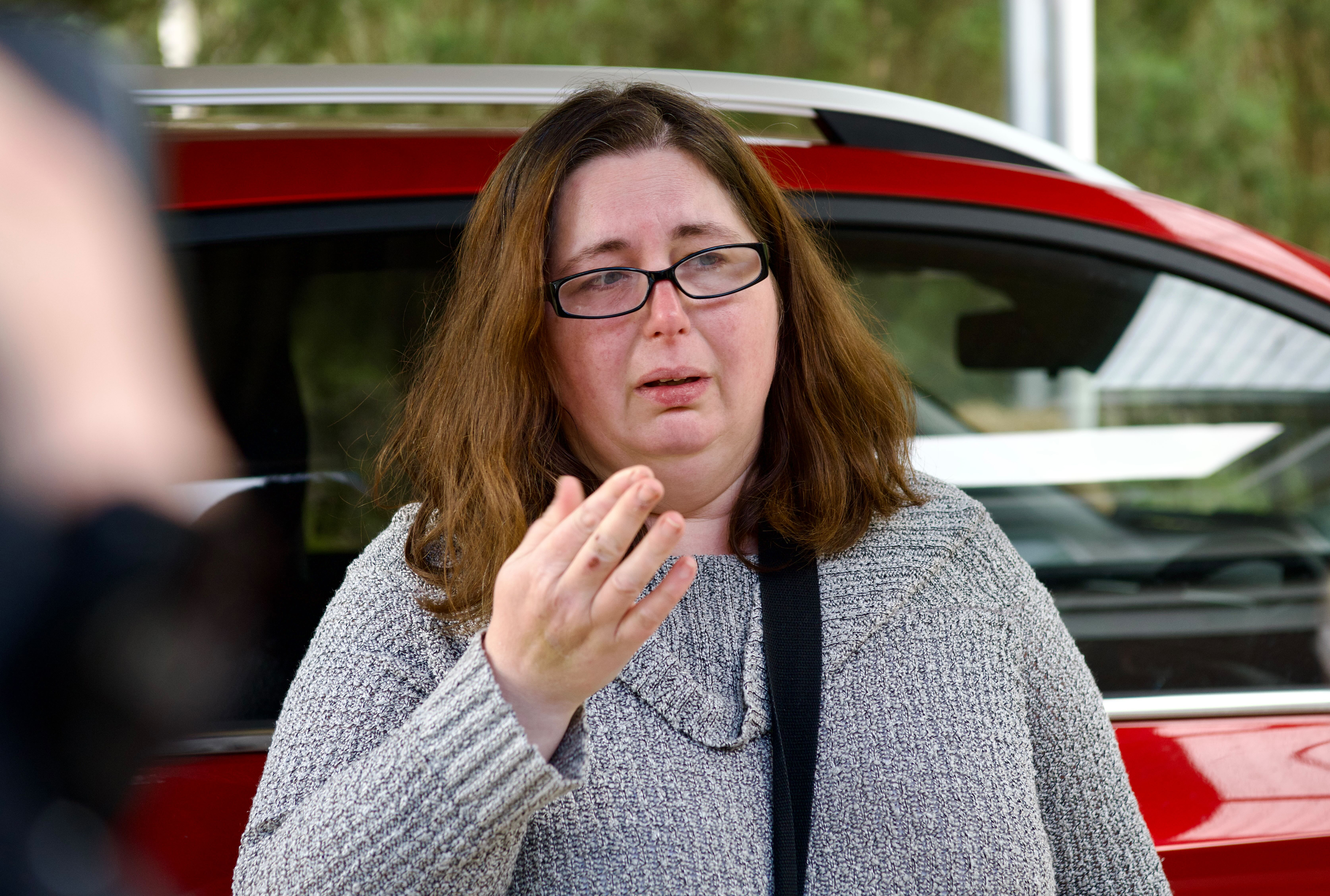 A woman with brown hair and wearing glasses standing beside her red car.