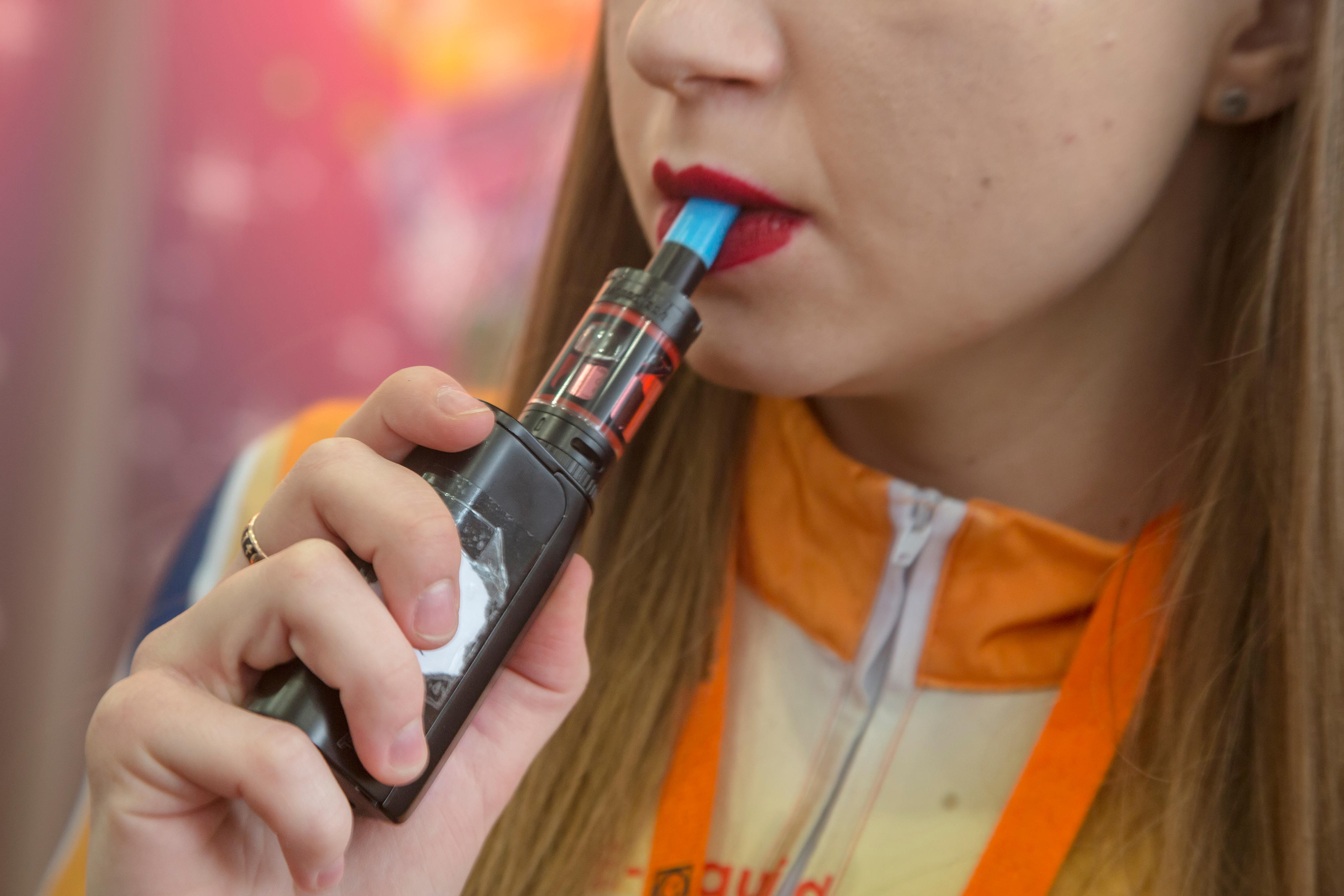 A young woman smokes an e-cigarette.