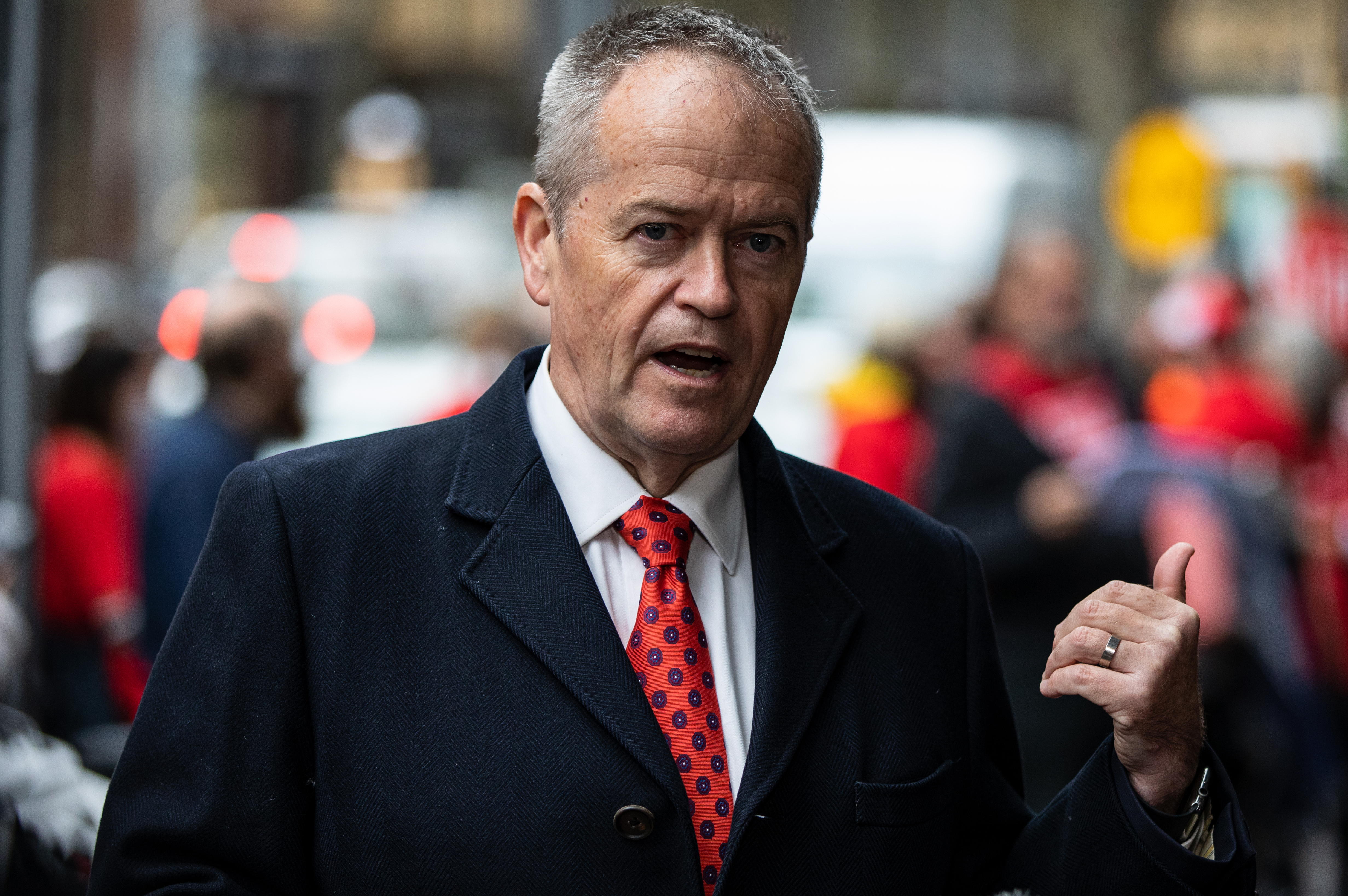 A middle-aged man speaks into microphones that surround him on the street.