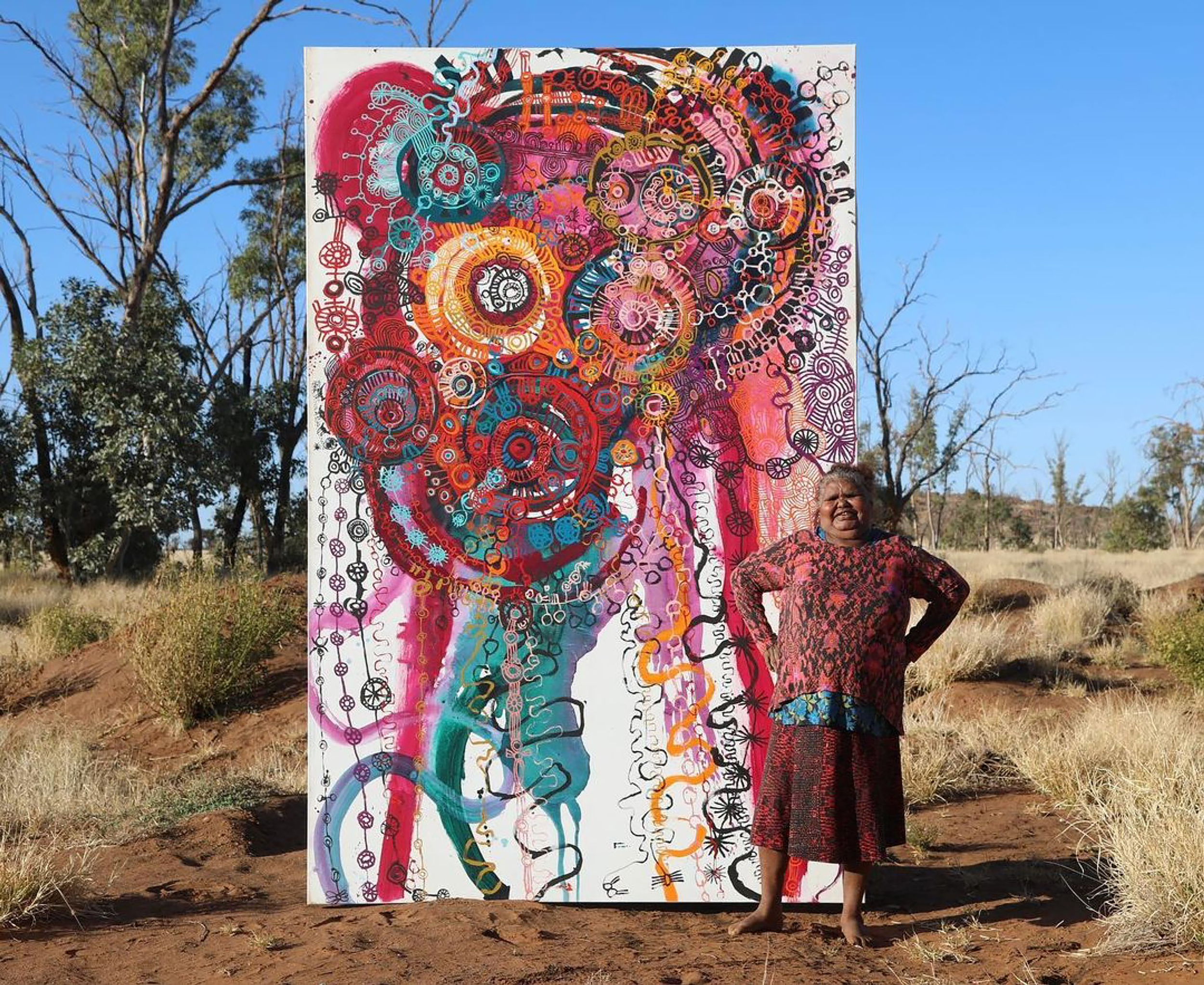 A woman stands beside a tall painting in the Australian outback.