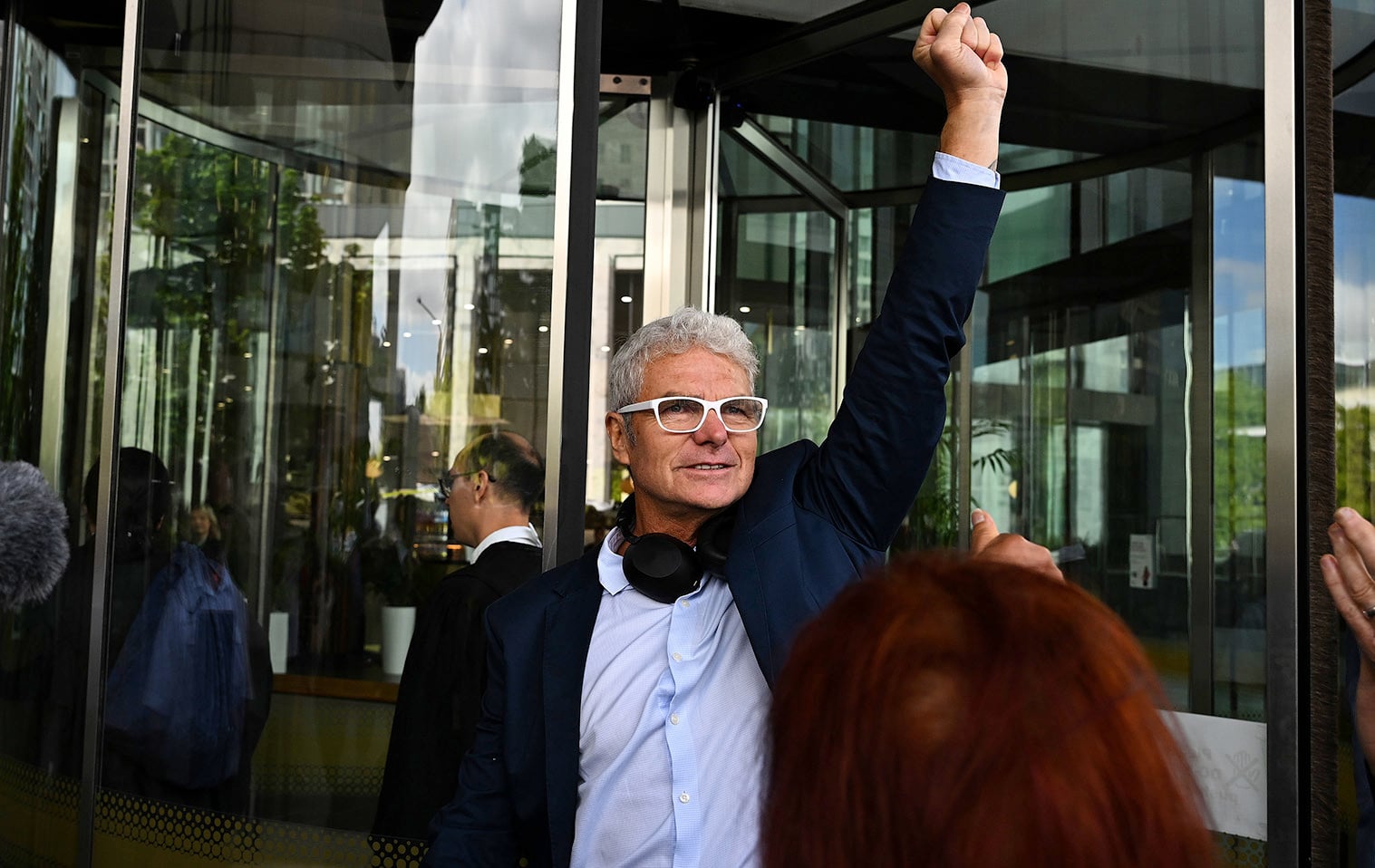 A man wearing a suit and glasses stands with his fist raised in the air.