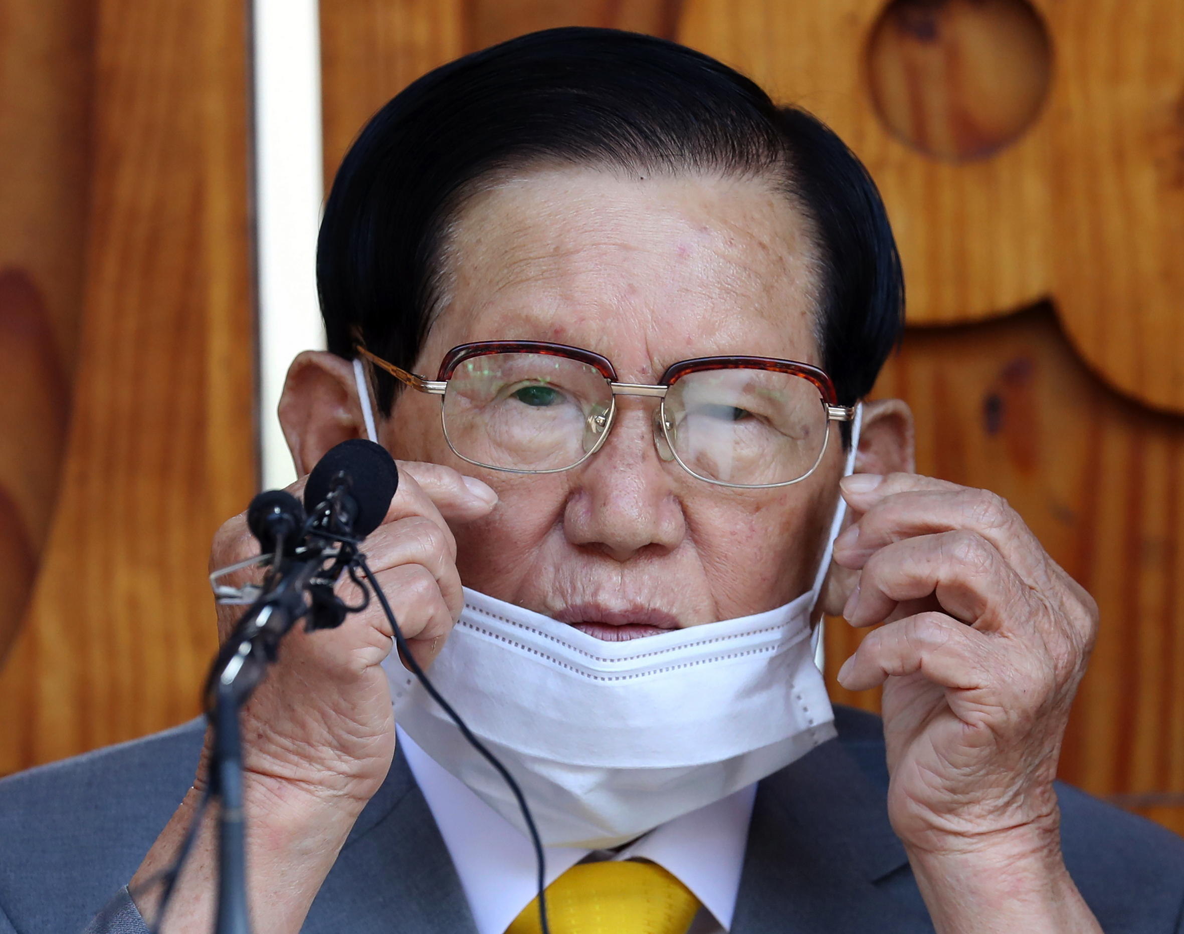 An elderly man lowers his mask to speak into a microphone.