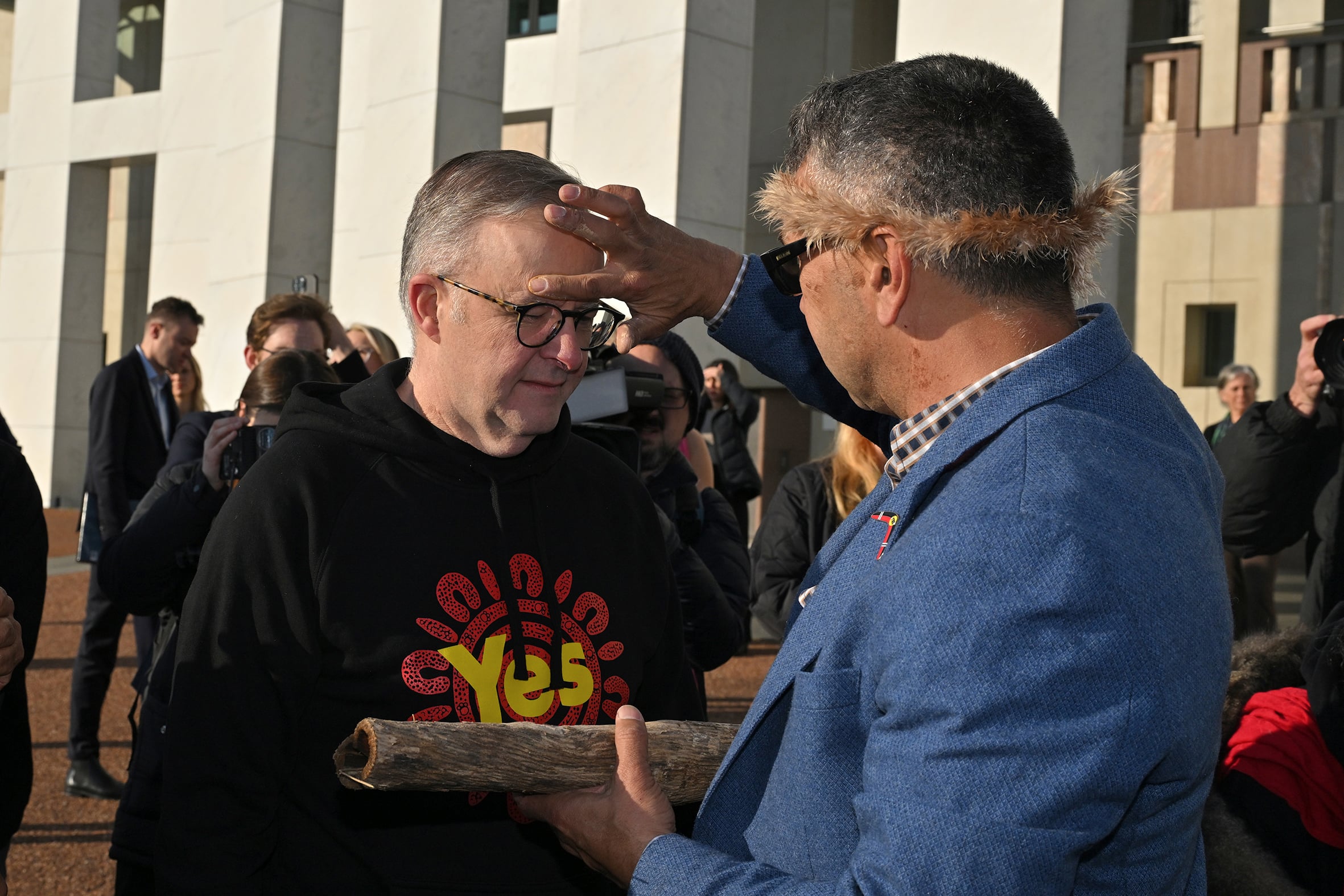 Prime Minister Anthony Albanese has ochre smeared on his forehead by a man in a blue blazer at Parliament House.