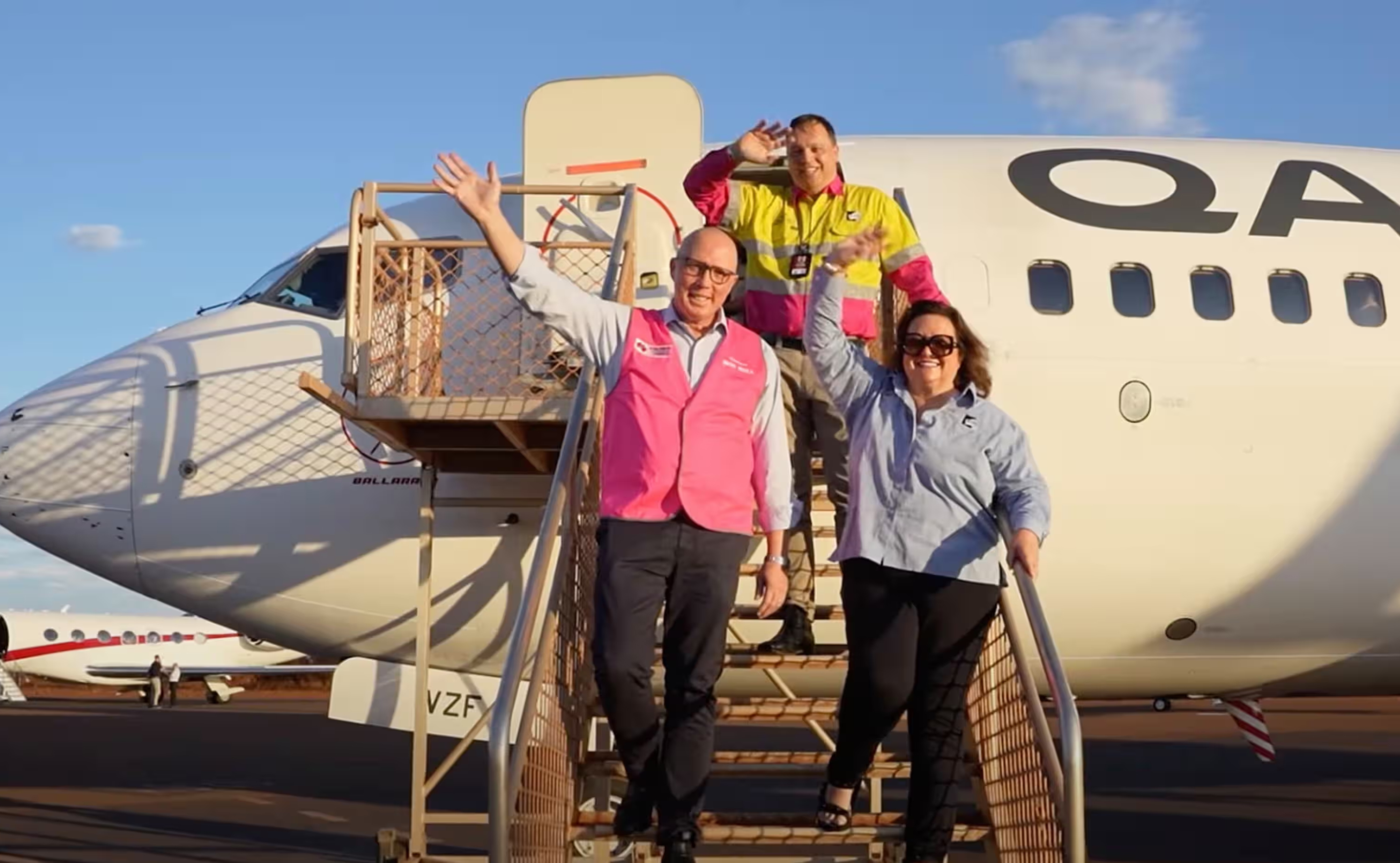 Peter Dutton and Gina Rinehart wave from the entrance to a Qantas airplane.