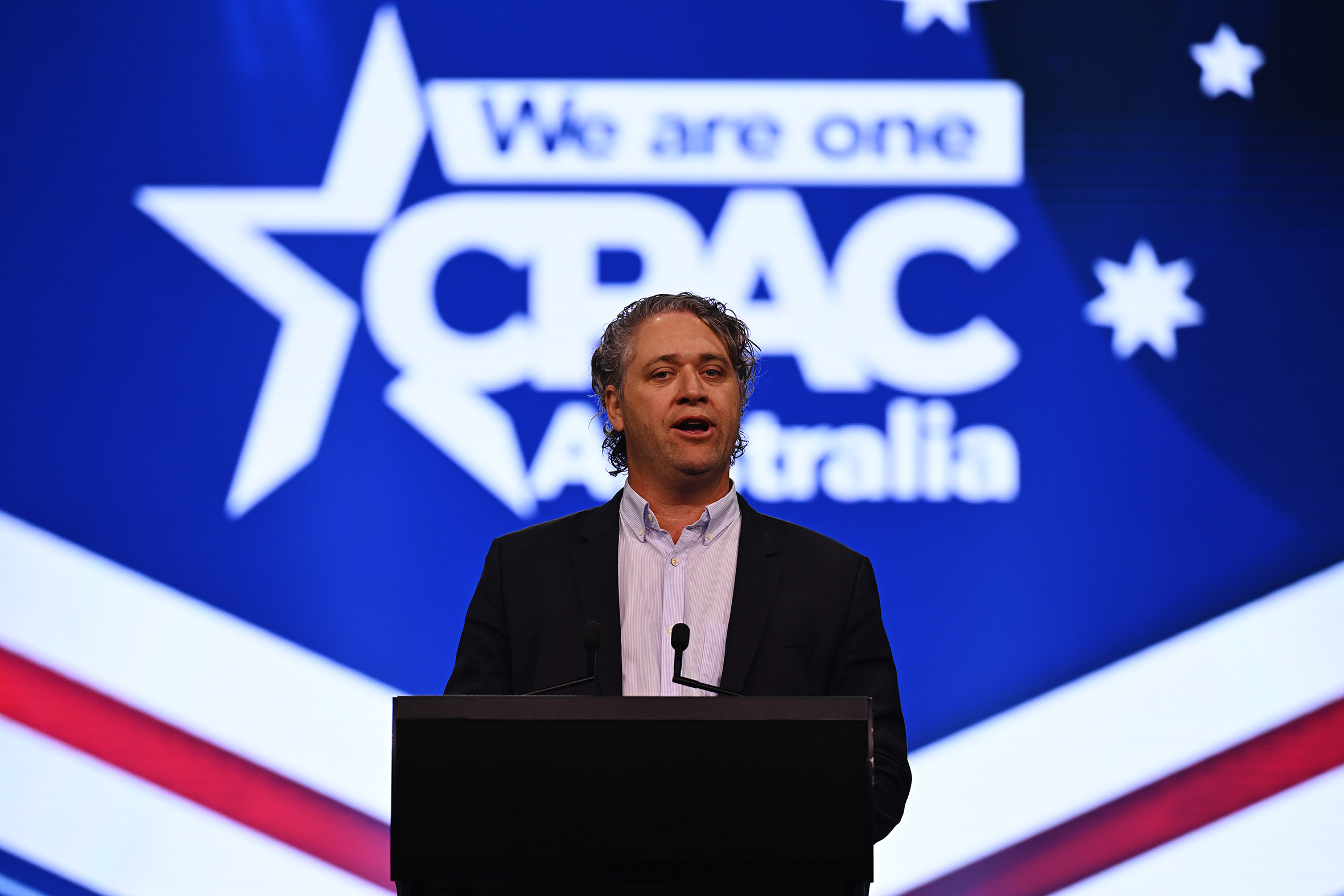 Am man with lock of grey hair and wearing a suit speaks at a conference.