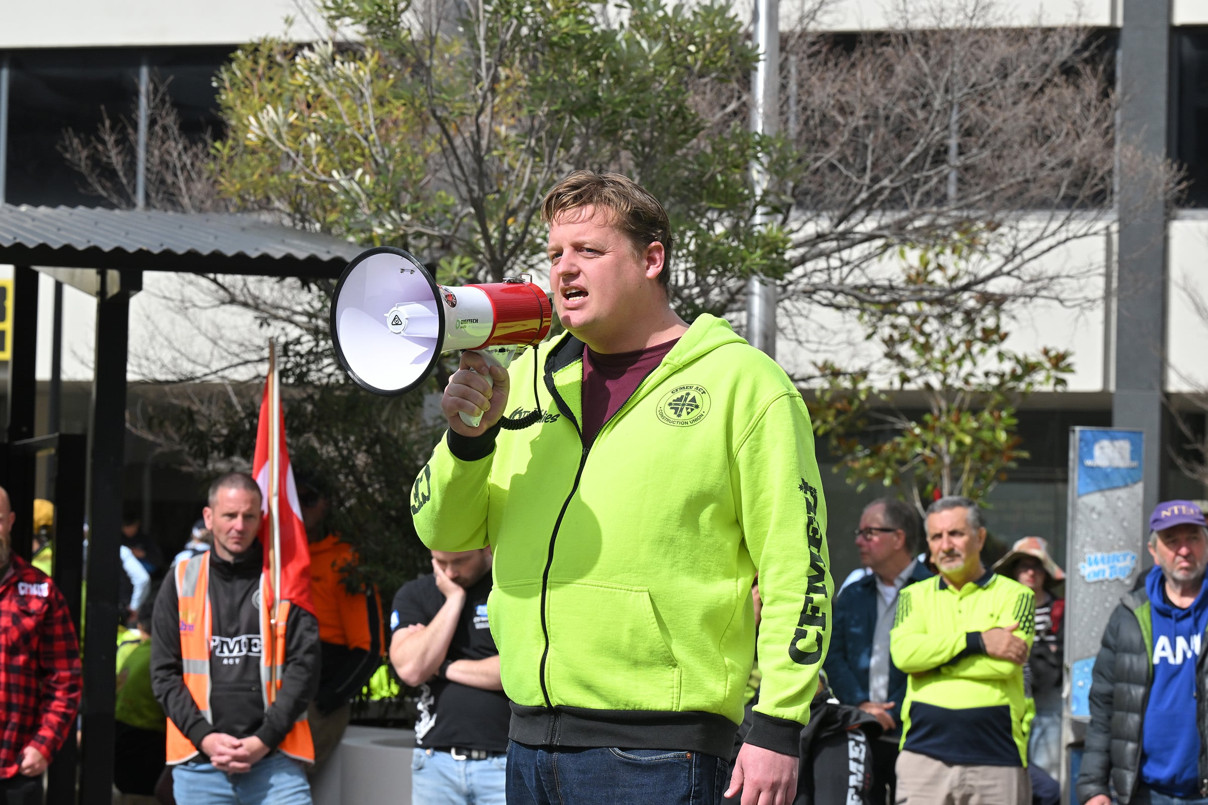Zach smith speak into a megaphone while wearing a bright green CFMEU jumper.