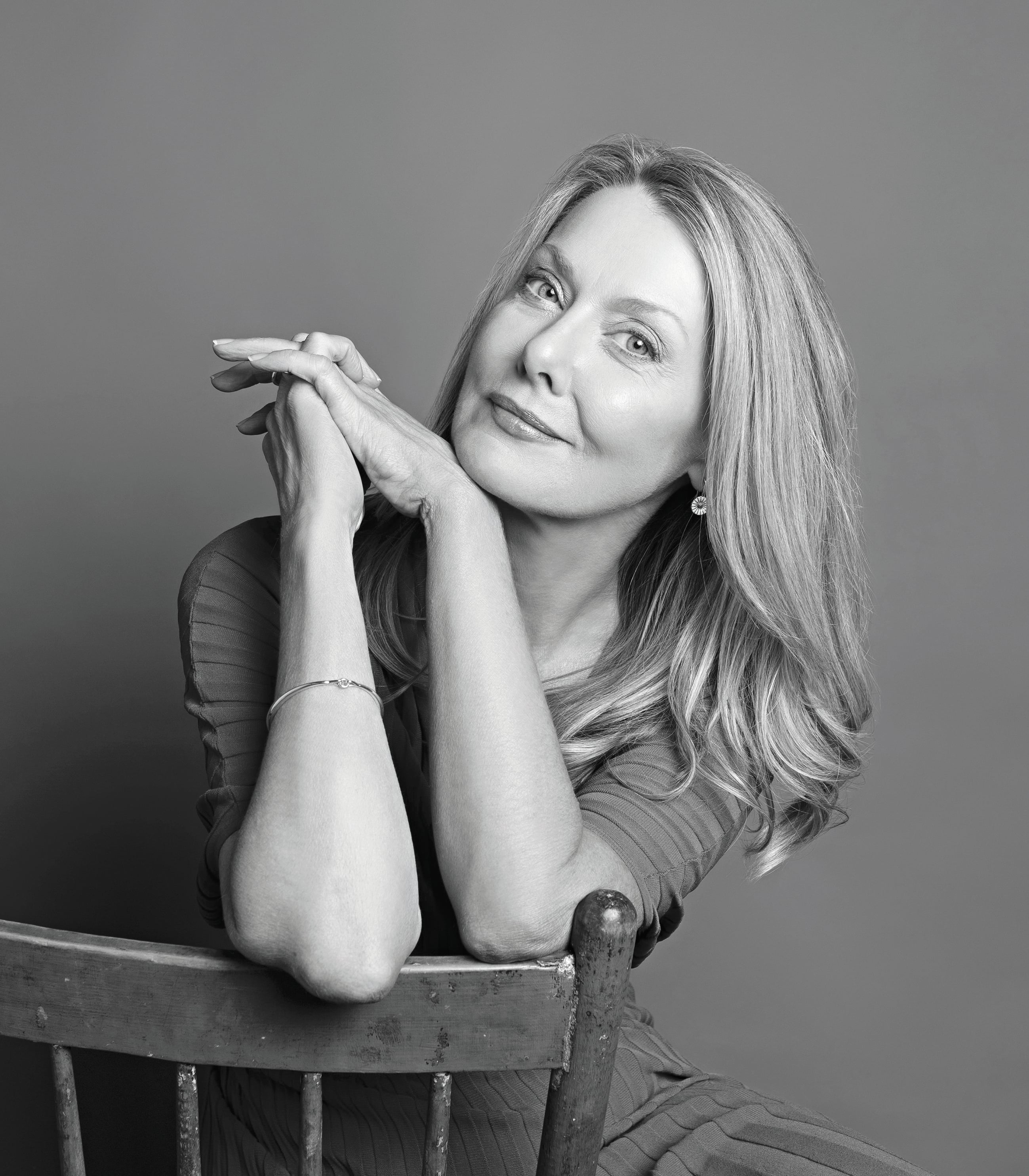 Greyscale portrait image of a blonde woman sitting backwards on a chair.