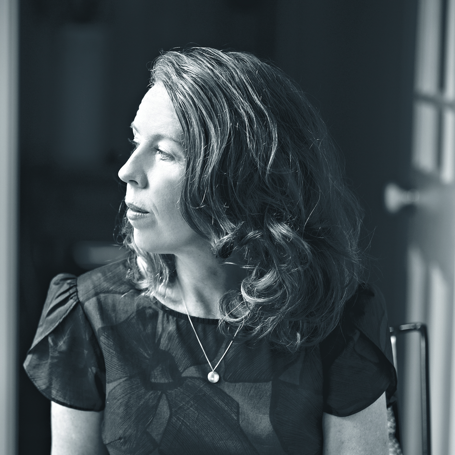 Greyscale portrait photograph of a middle-aged woman with dark brown wearing a deep blue dress. 