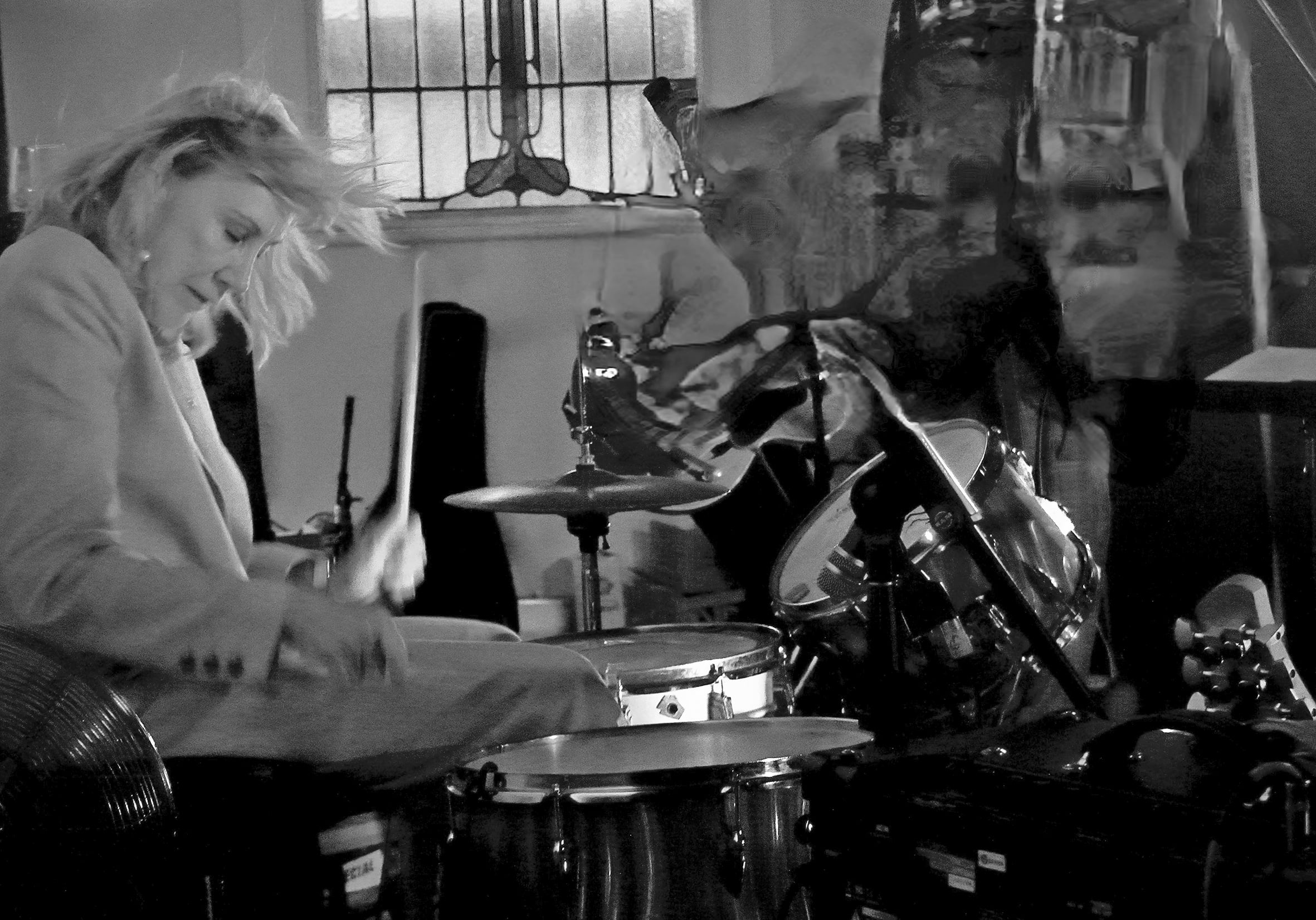 A woman dressed in a blazer playing the drums.