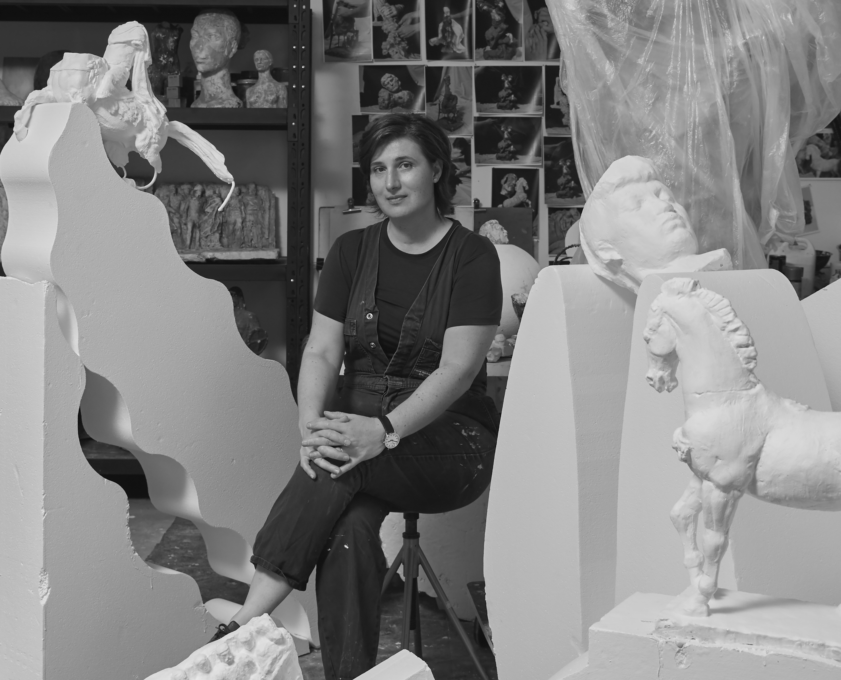 An artist sits among on a stool surrounded by her sculptures.