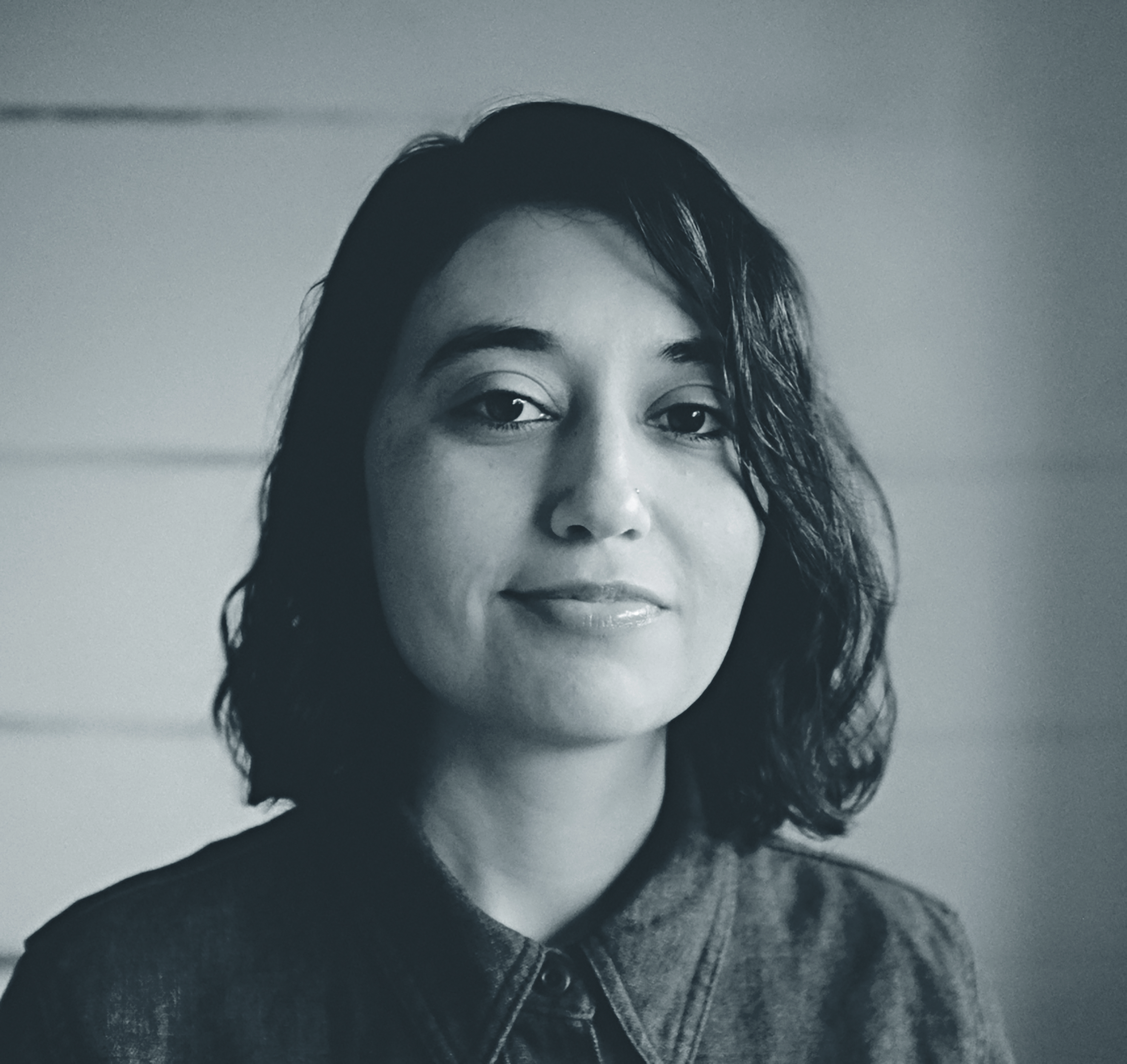 Greyscale portrait photograph of a young woman with dark hair and a nose piercing.