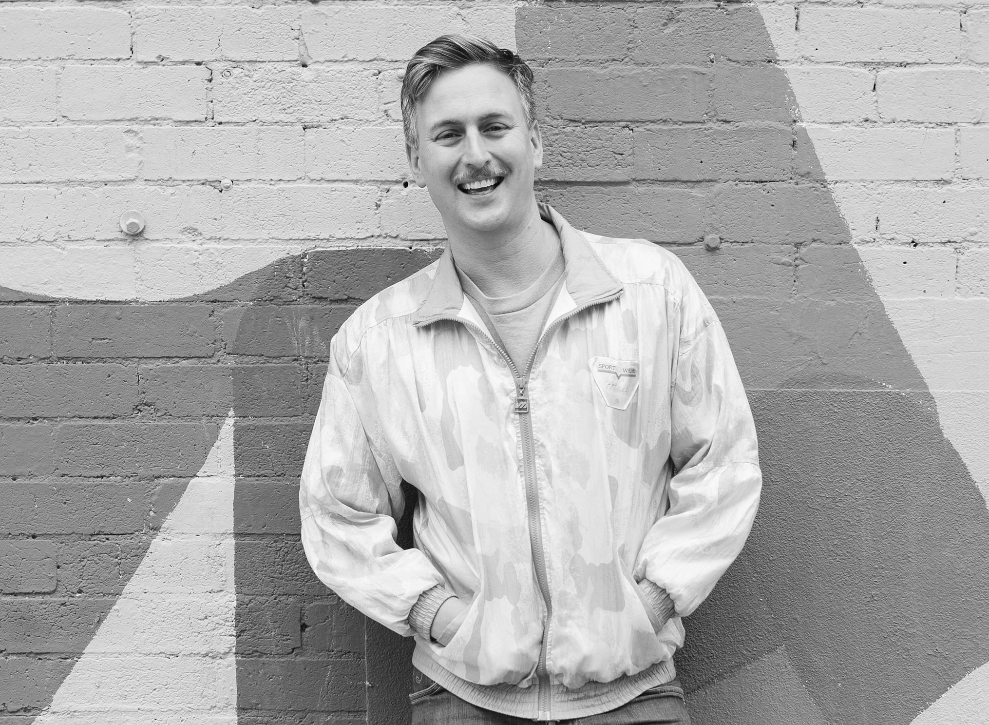 Greyscale portrait photograph of a man with a moustache dressed in a bomber jacket.