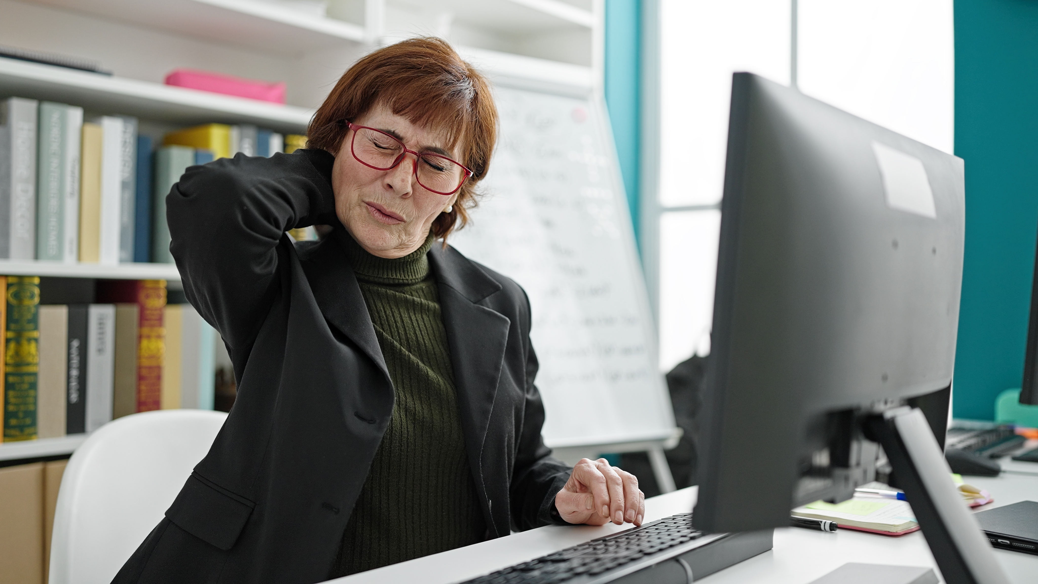 An office worker rubbing their neck as they sit at a computer desk.