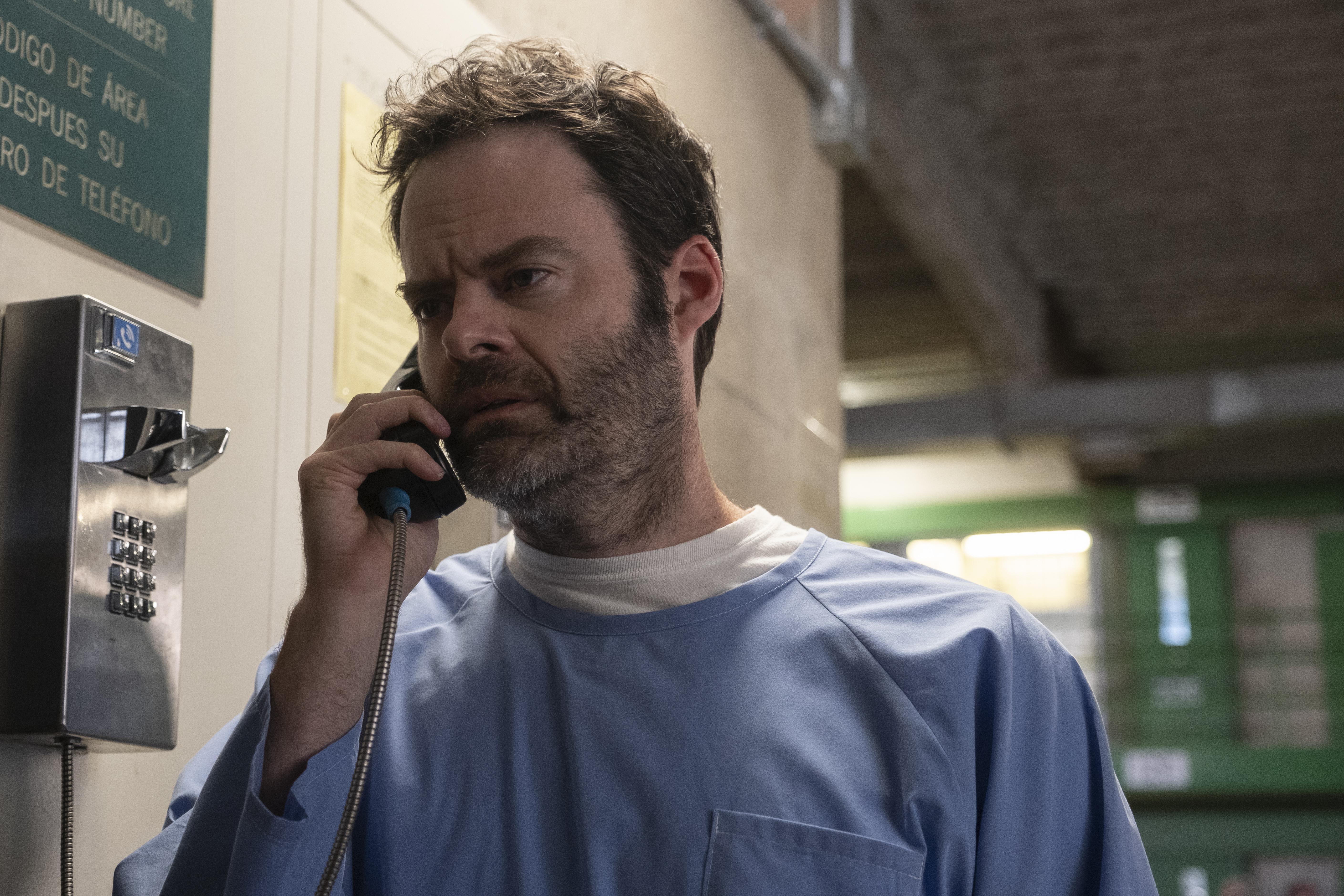 A man in a blue hospital robe speaks on a payphone