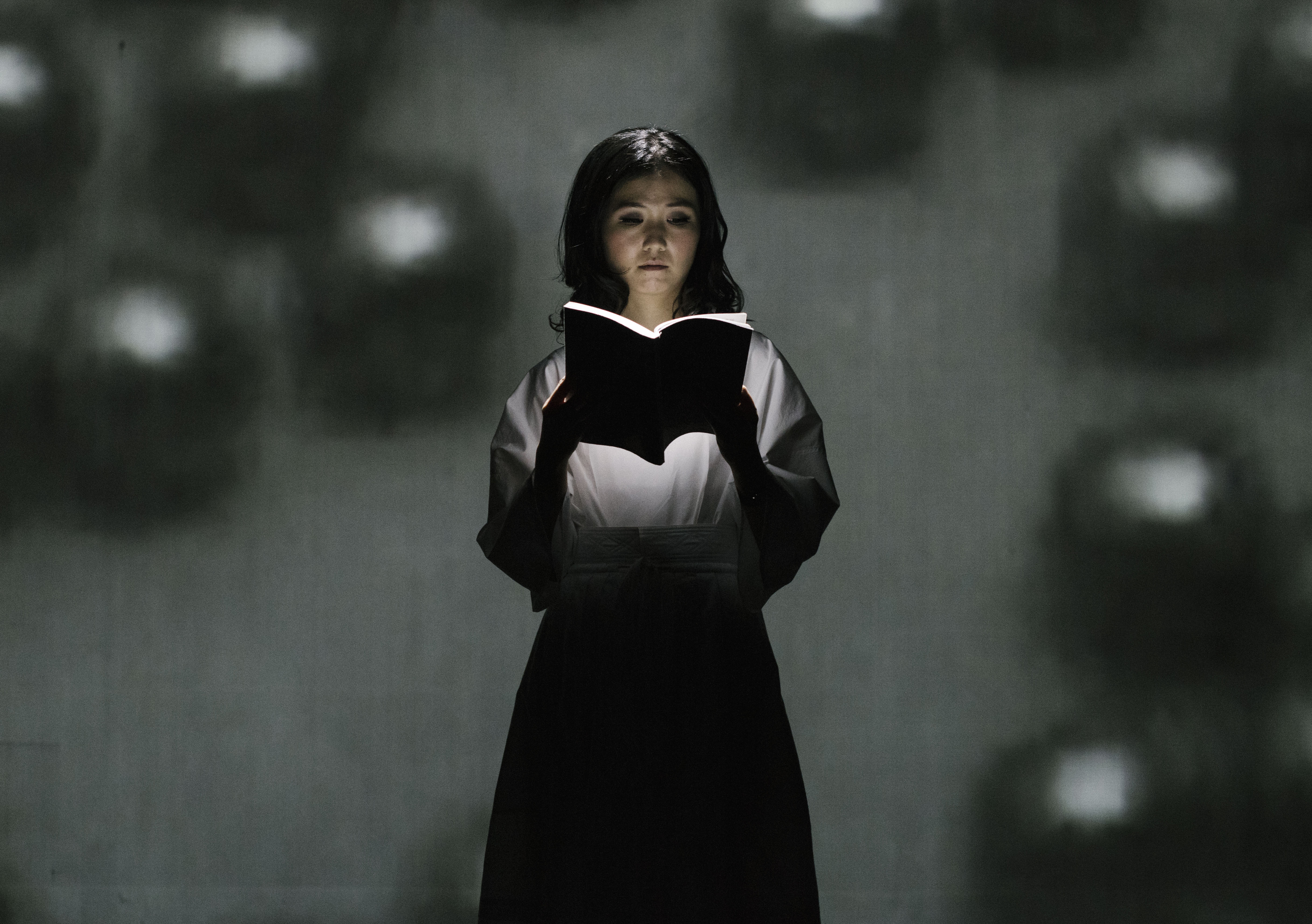 A woman reading a book as she stands under a spotlight. 