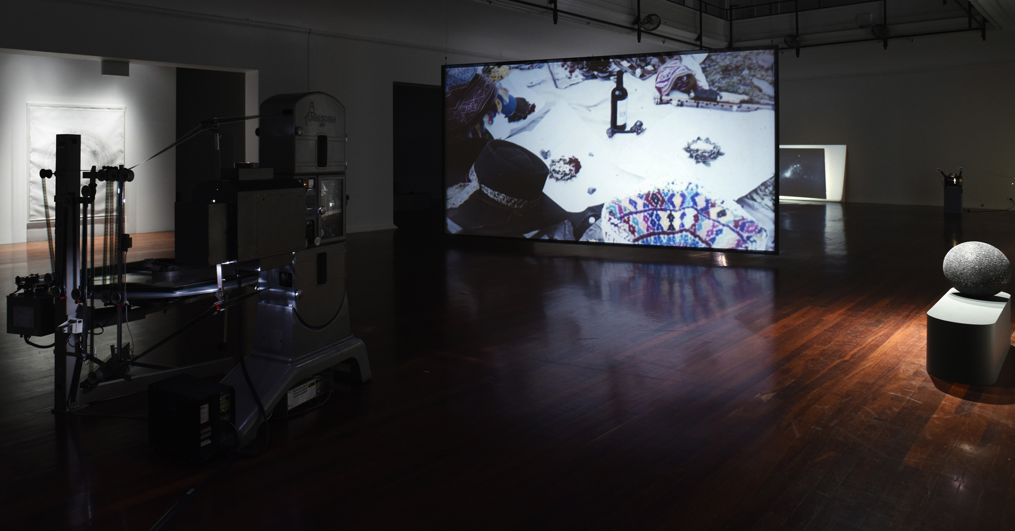 A large room with wooden floorboards and a projection of an art installation in the centre.