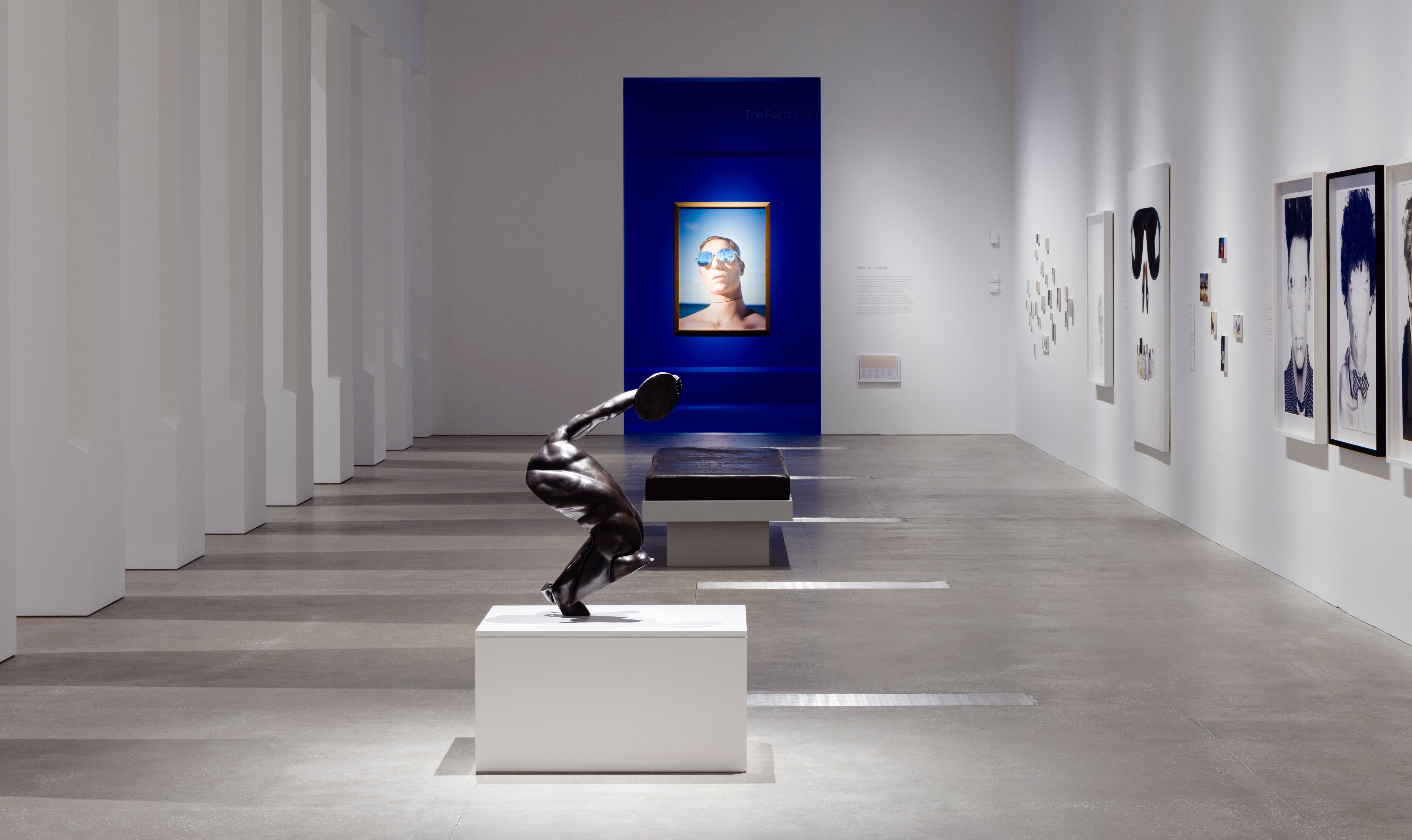 An exhibition featuring a statue and several portrait photographs on the walls.
