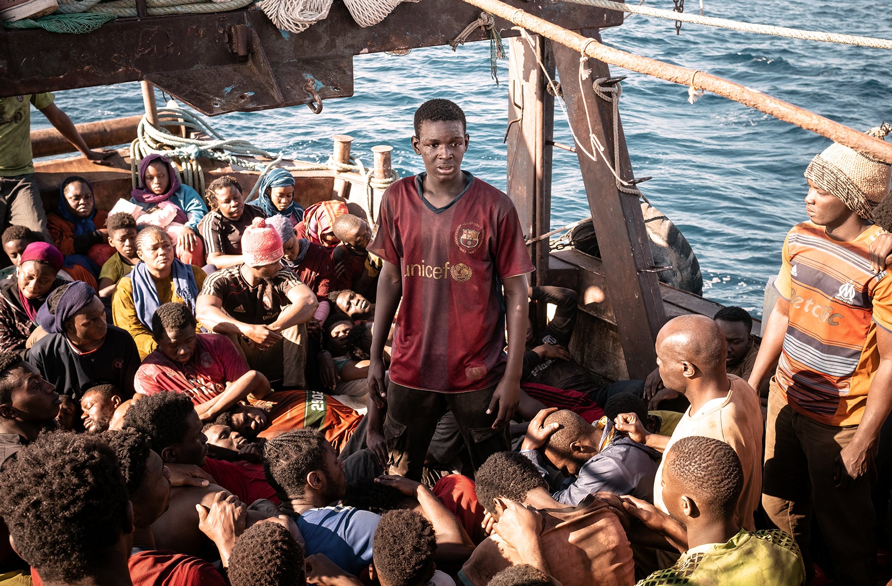 A young man stands in the middle of an overcrowded boat.