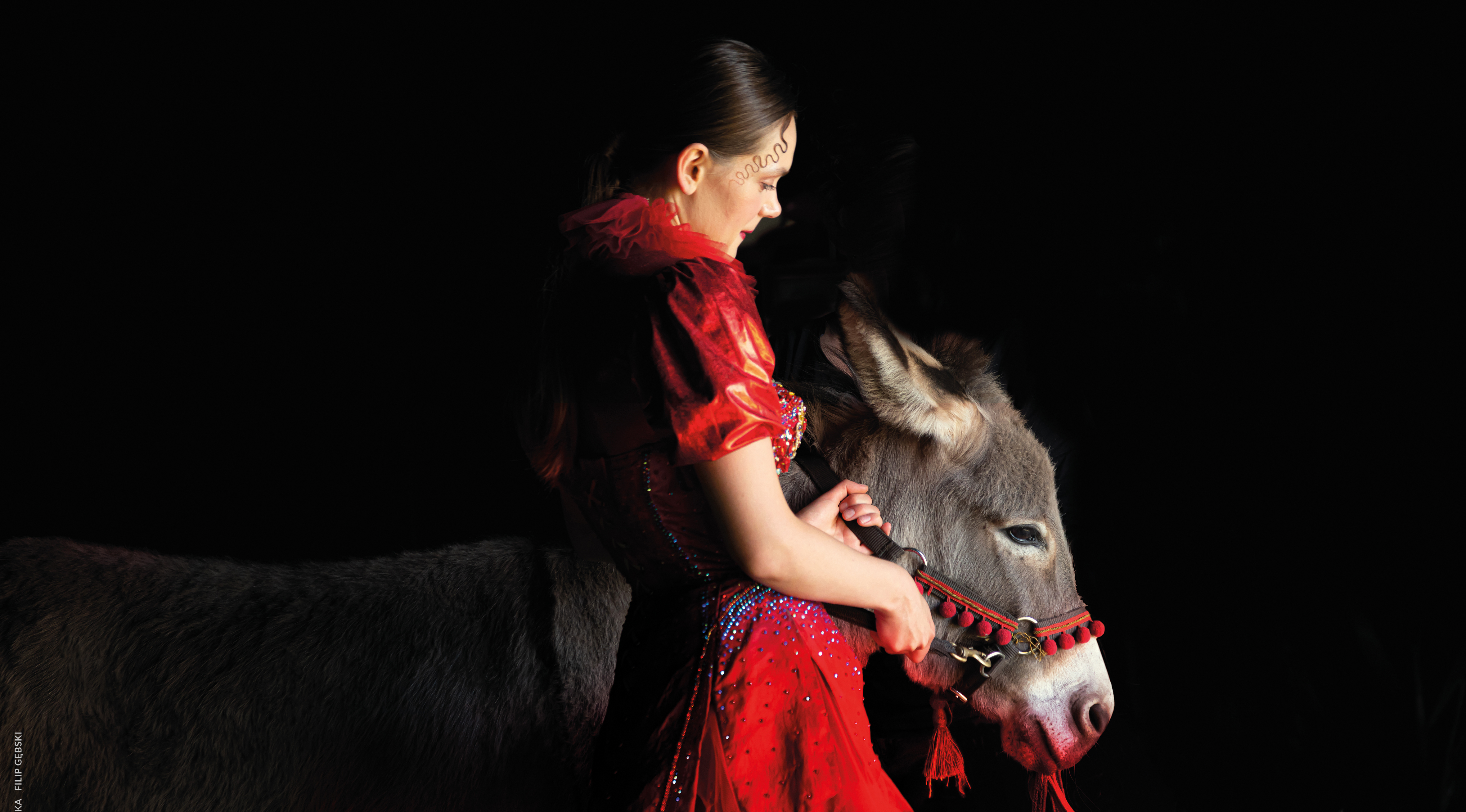 Sandra Drzymalska in red dress, holding onto a donkey by the saddle.