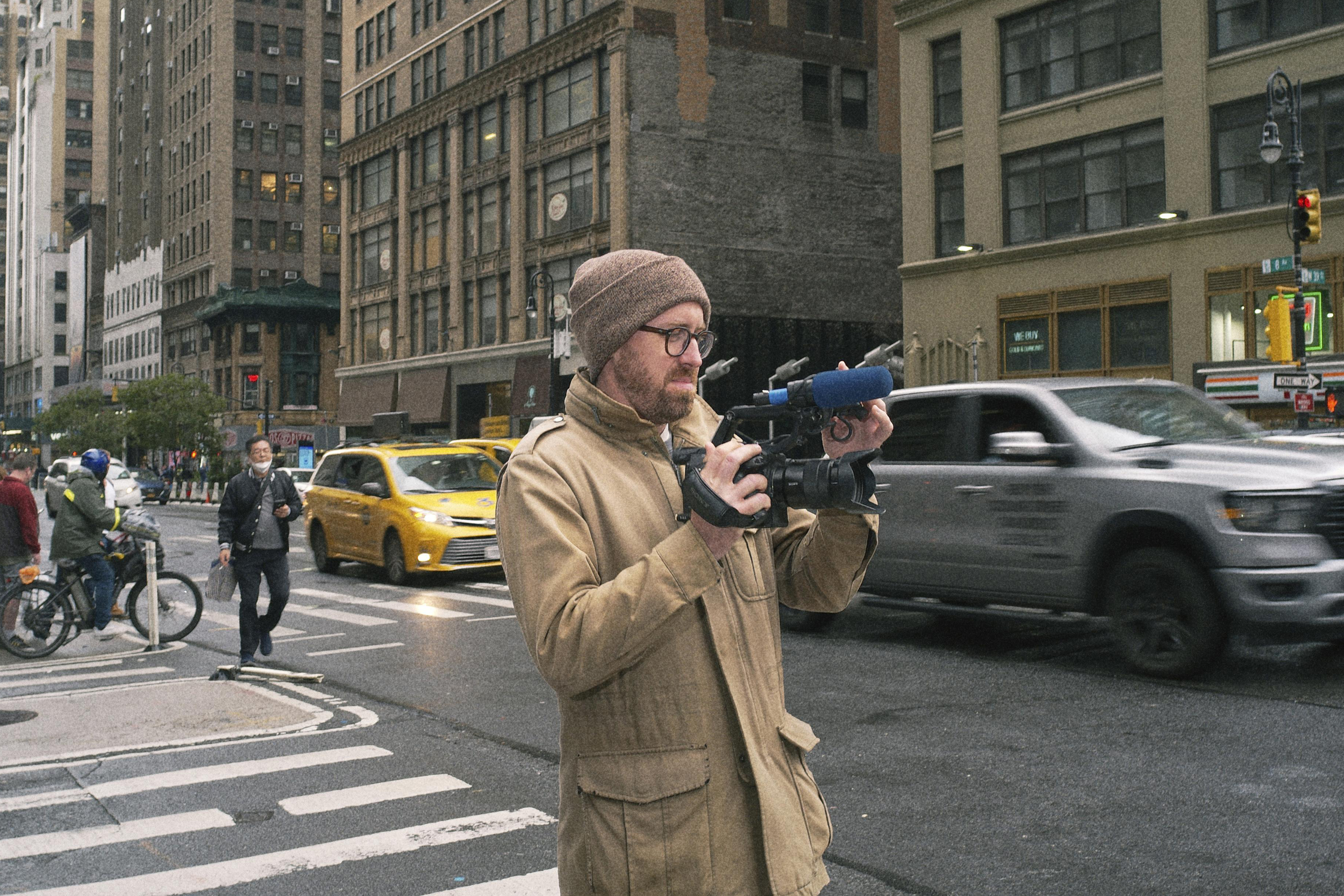 A man films a busy city street from the footpath.