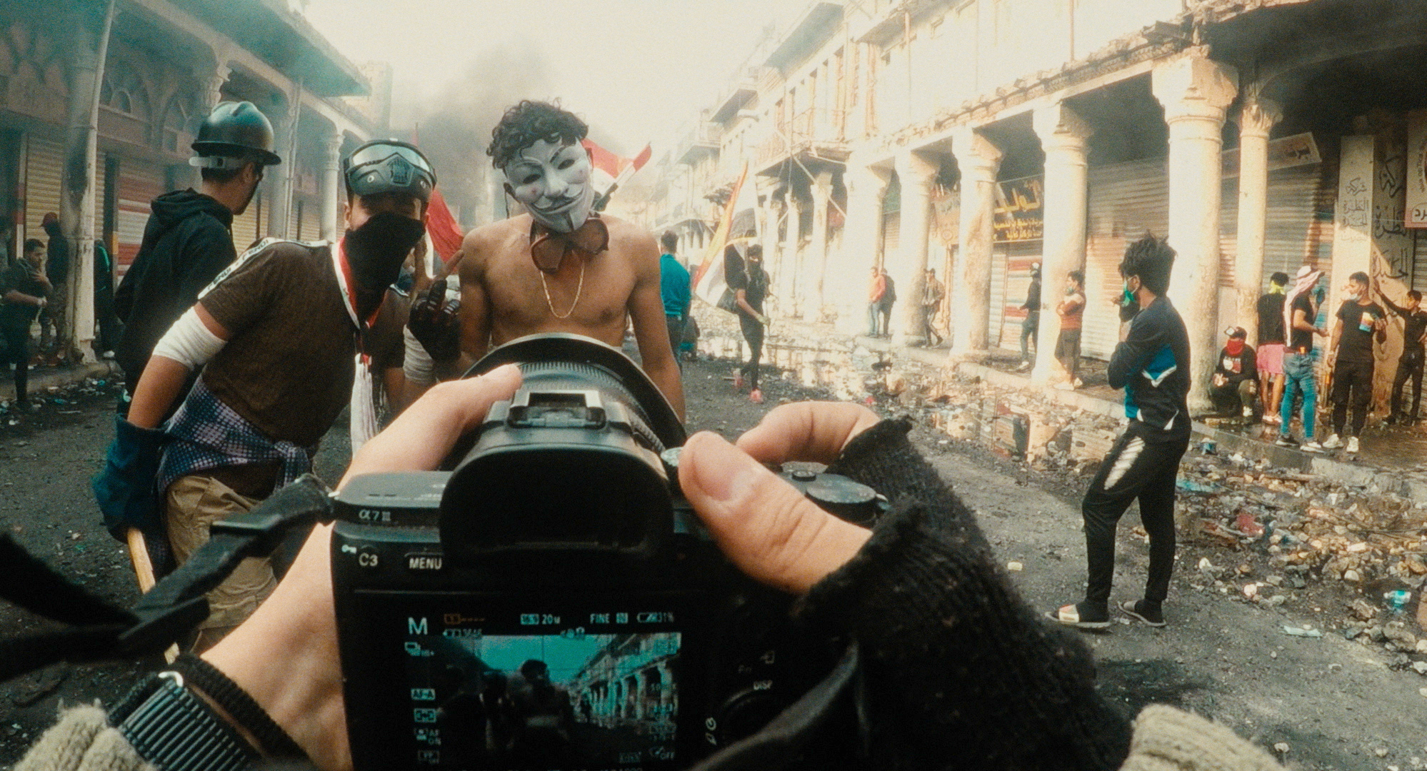 In a scene from Maja Tschumi’s Immortals, two Iraqi protestors pose in front of a camera, one wears a mask.