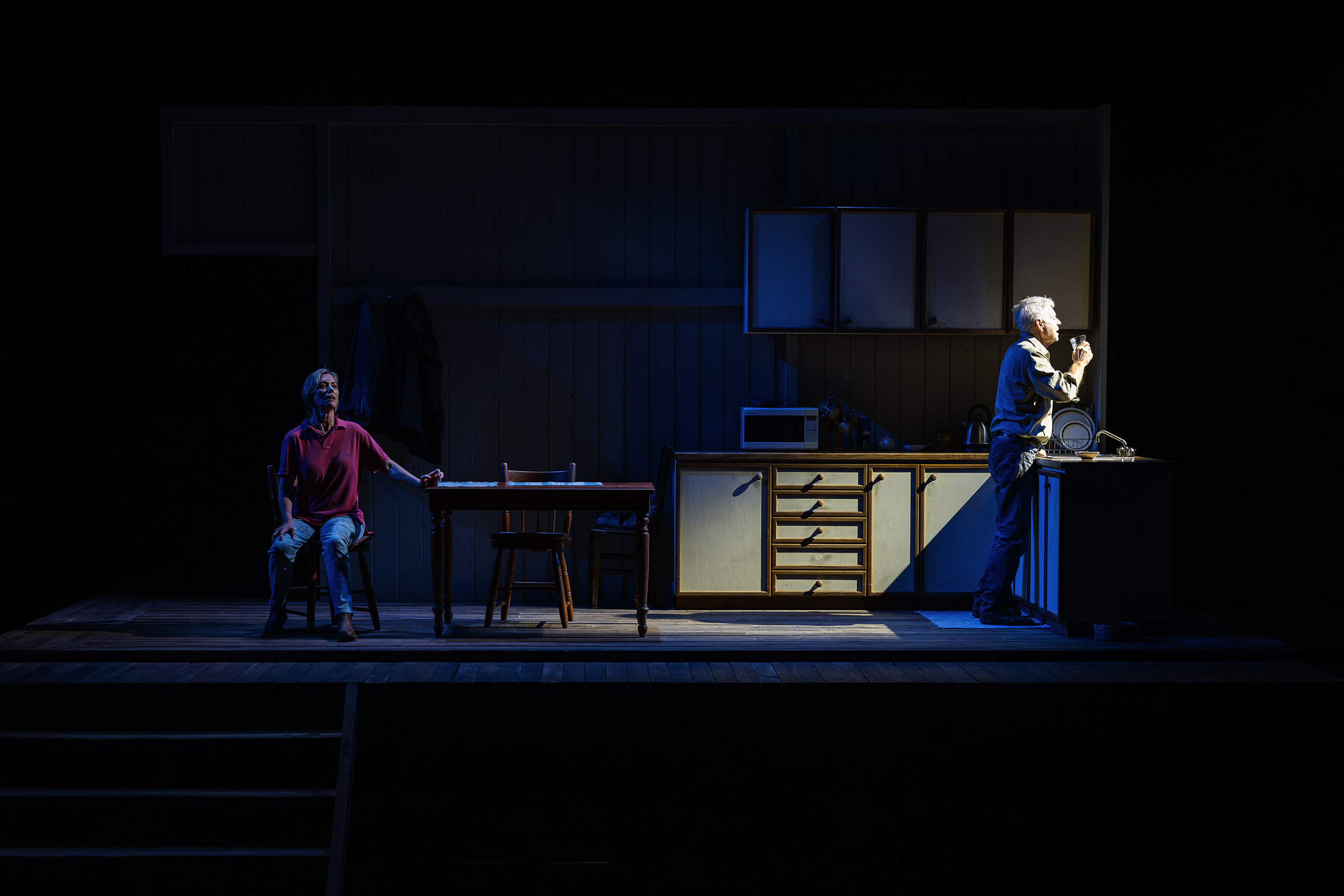 Two actors perform in a kitchen set on stage.