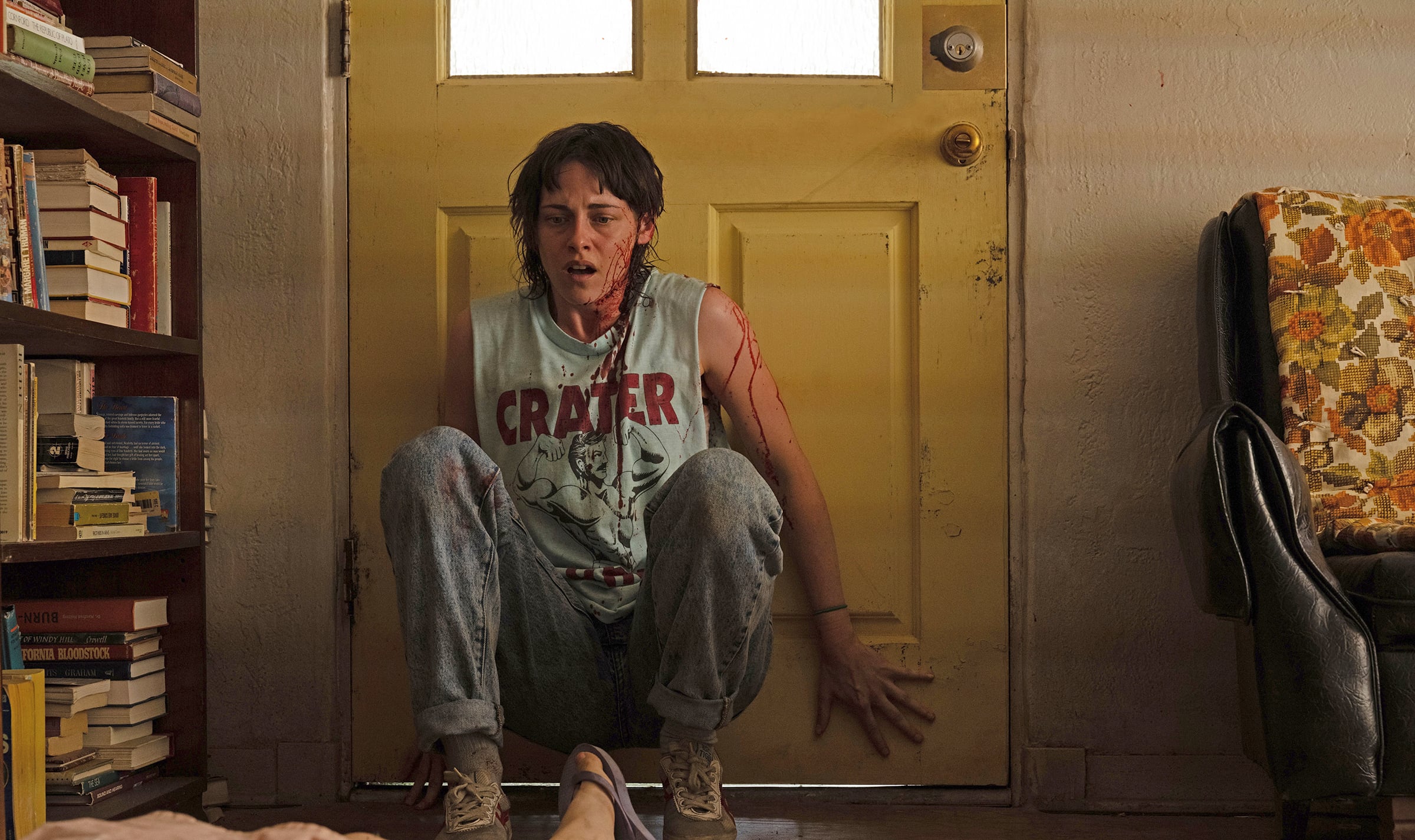 Kristen Stewart leans against a door with blood over her clothes.