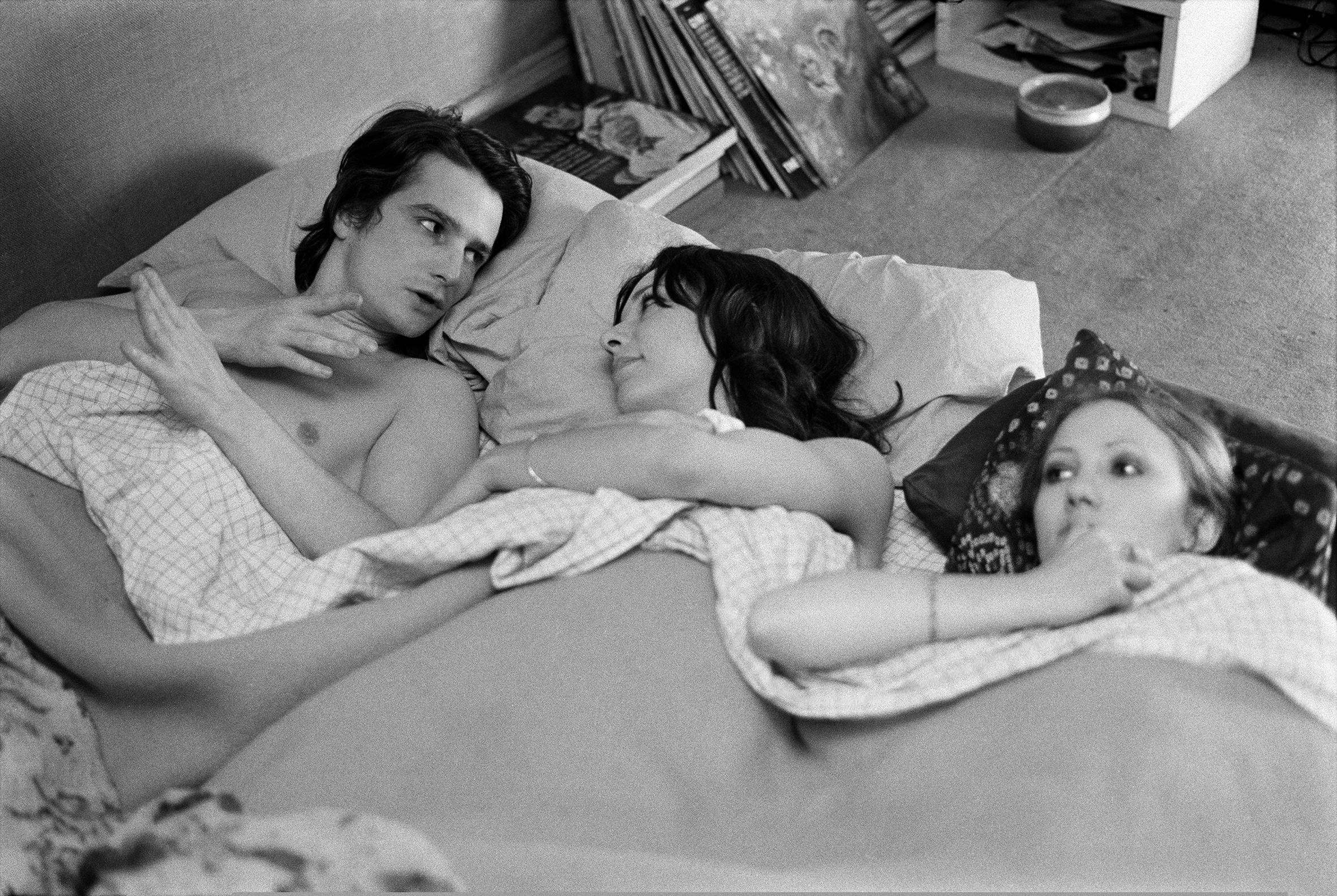 Three people resting topless in a bed.